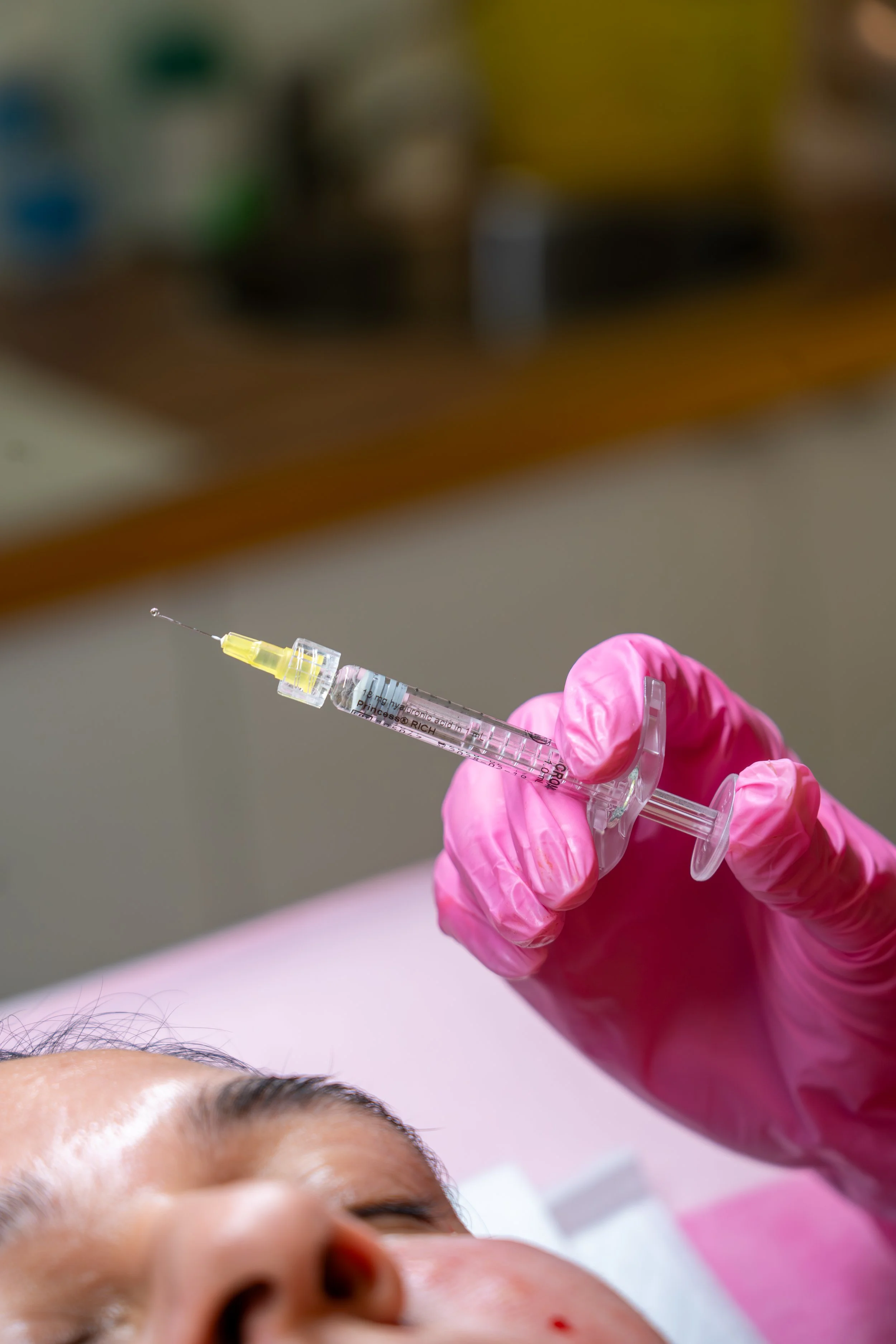 A person wearing pink gloves administering a vaccination to a person's face.