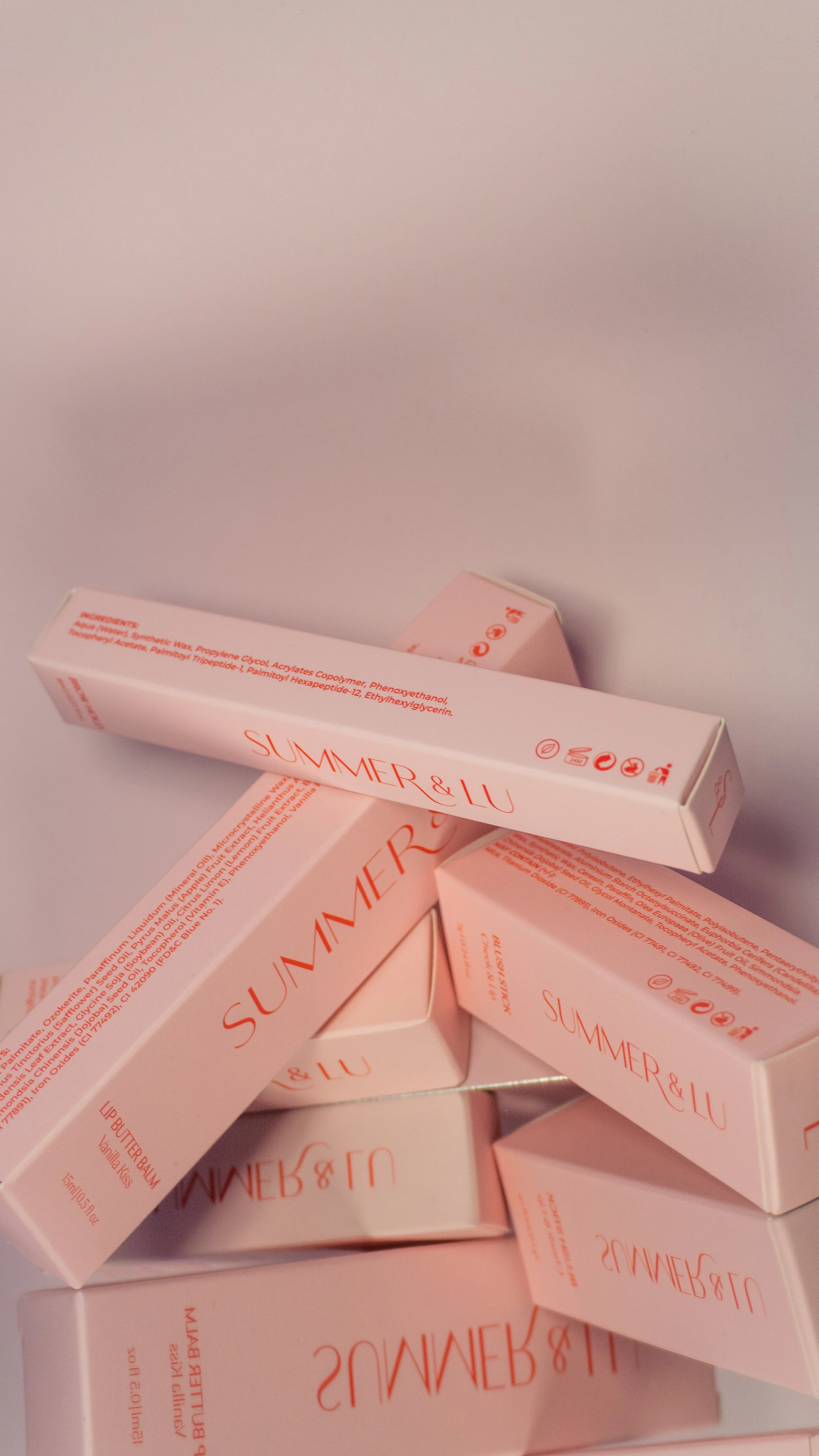 Multiple pink boxes of Lip Butter Balm with the label 'Summer & Lu' stacked on each other against a plain background.