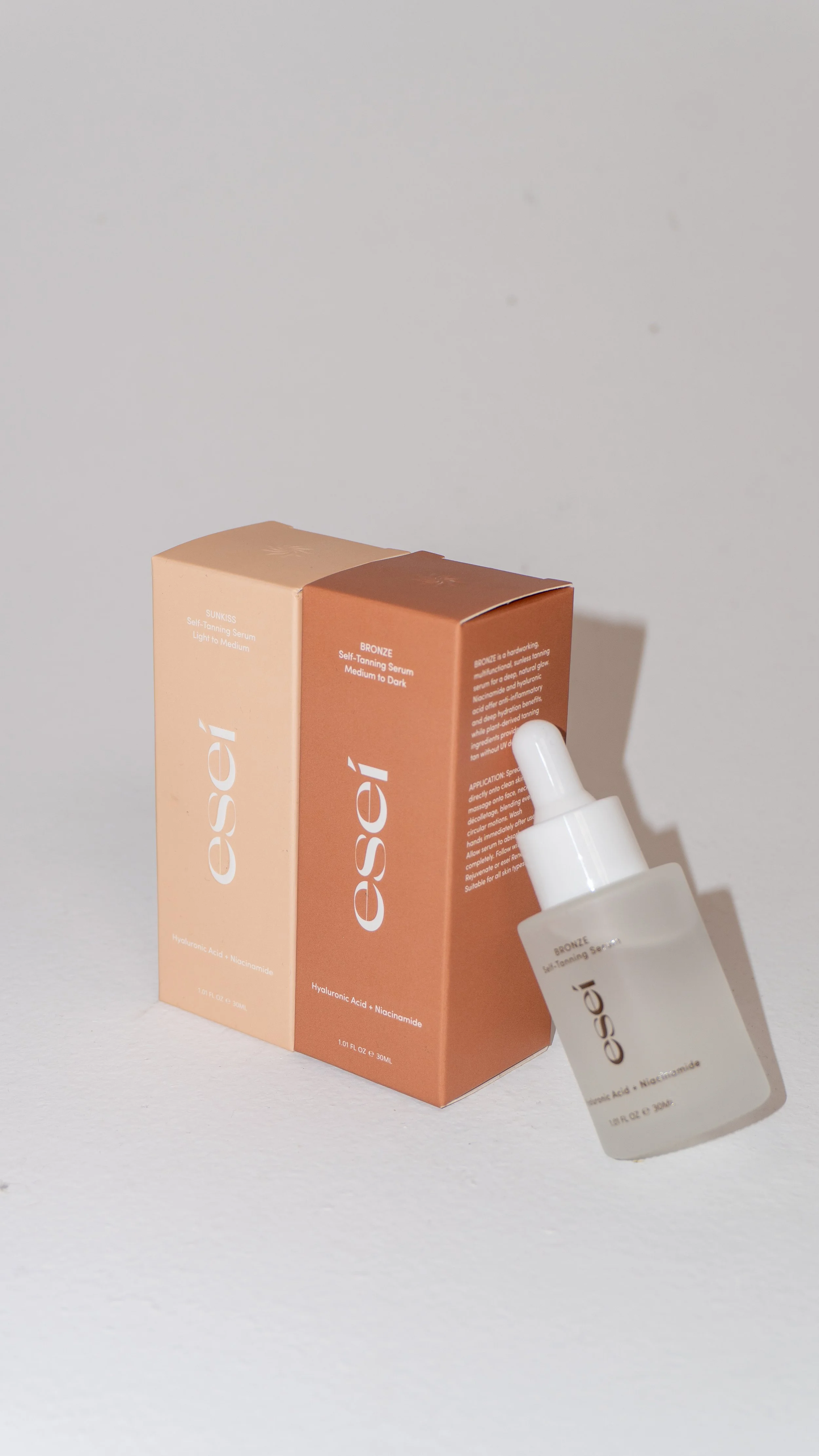 Esamself-branded self-tanning serum product with a dropper, placed next to its two-tiered packaging box in shades of beige and bronze.