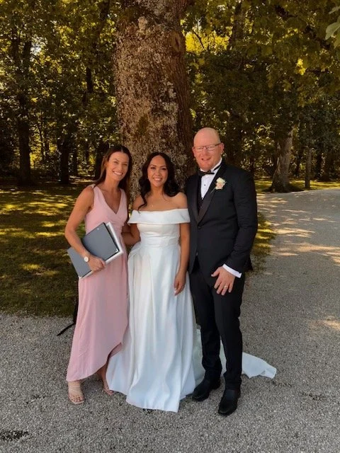 Celebrant Ollie van der Pol smiling as she leads the ceremony for a couple at Bangor Farm, oak trees framing the background.