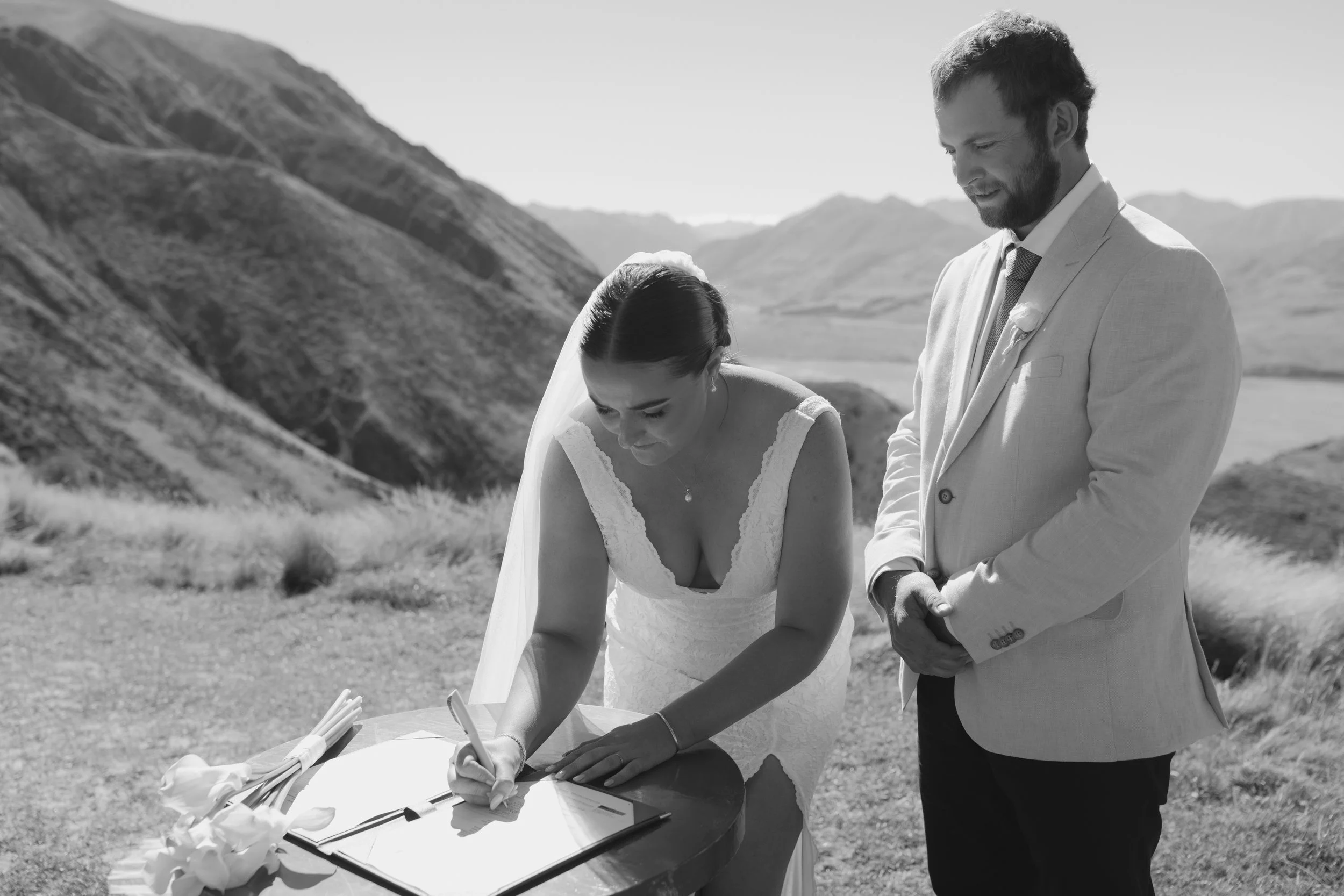 Bride and groom signing their marriage documents with the Southern Alps in the background.