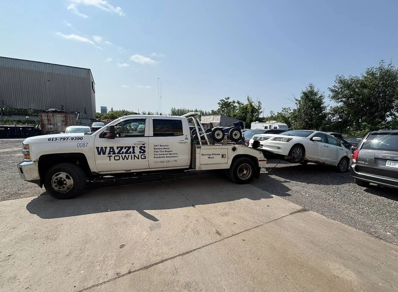 Wazzi's Towing truck towing a white sedan in a parking lot on a sunny day.