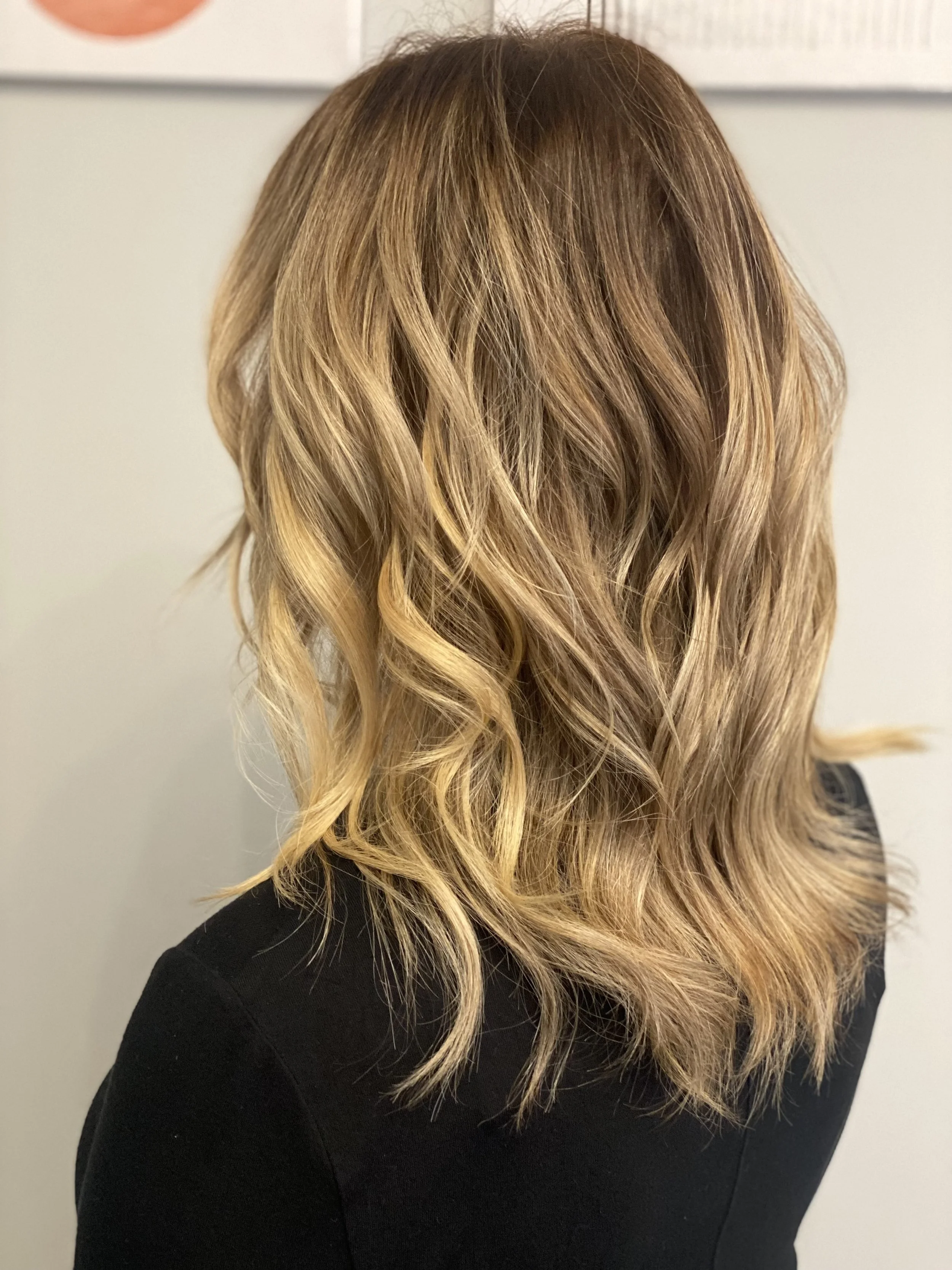 Wavy blonde hair viewed from the back, worn with a black top.