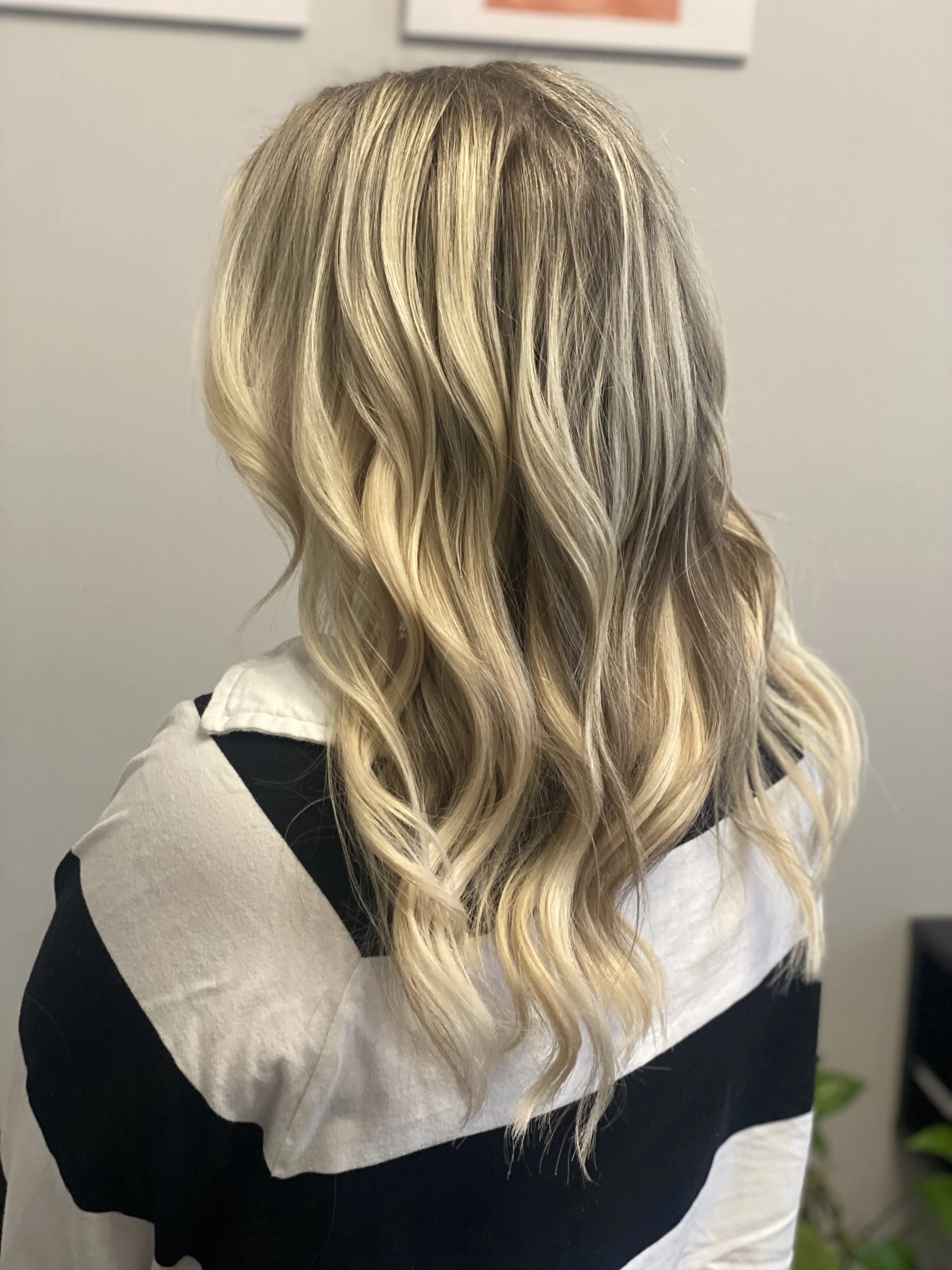 Back view of a woman with long, blonde, wavy hair wearing a black and white top.