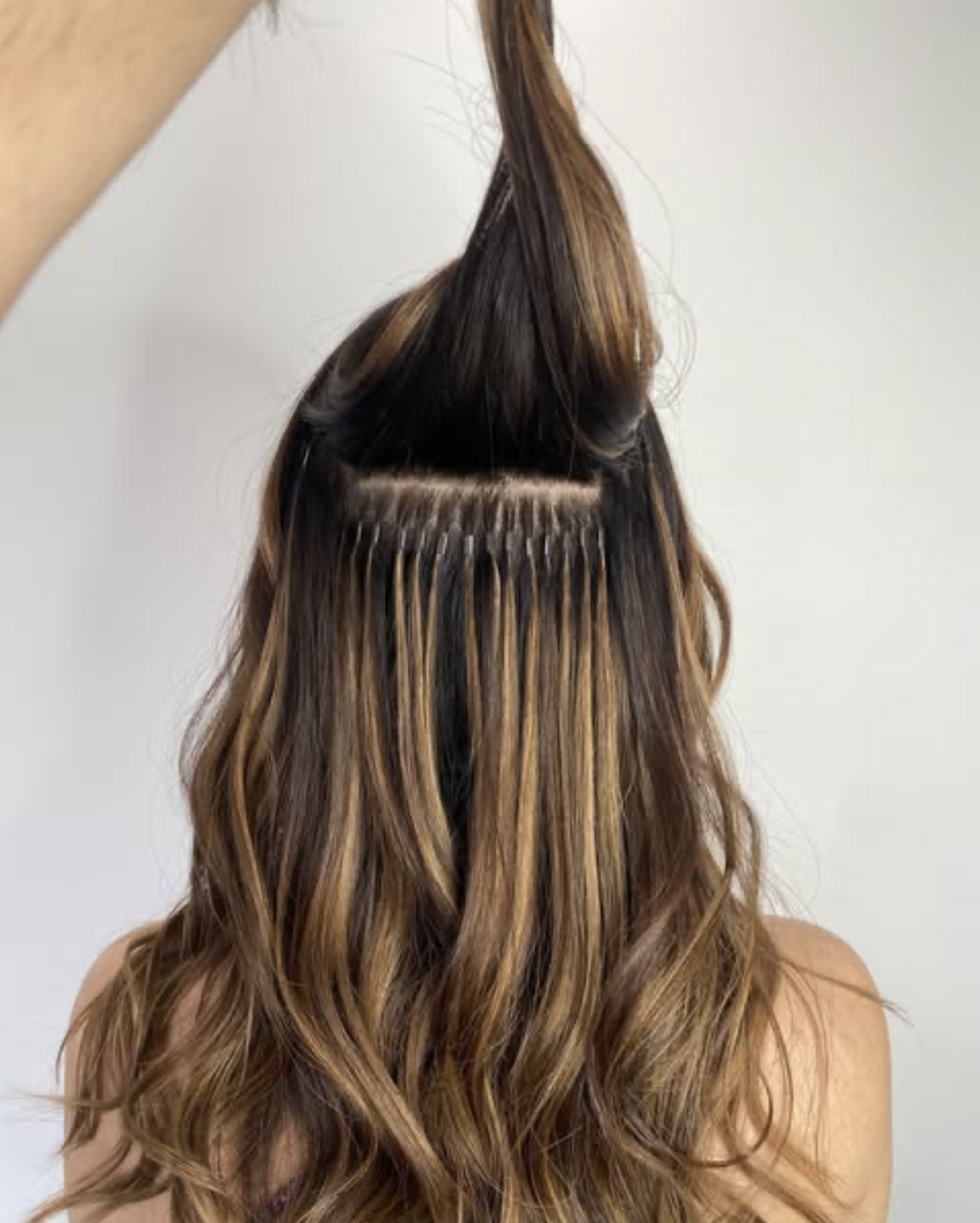 Hair extensions being applied to a person's hair, showing a close-up view of the process with the person's back facing the camera.
