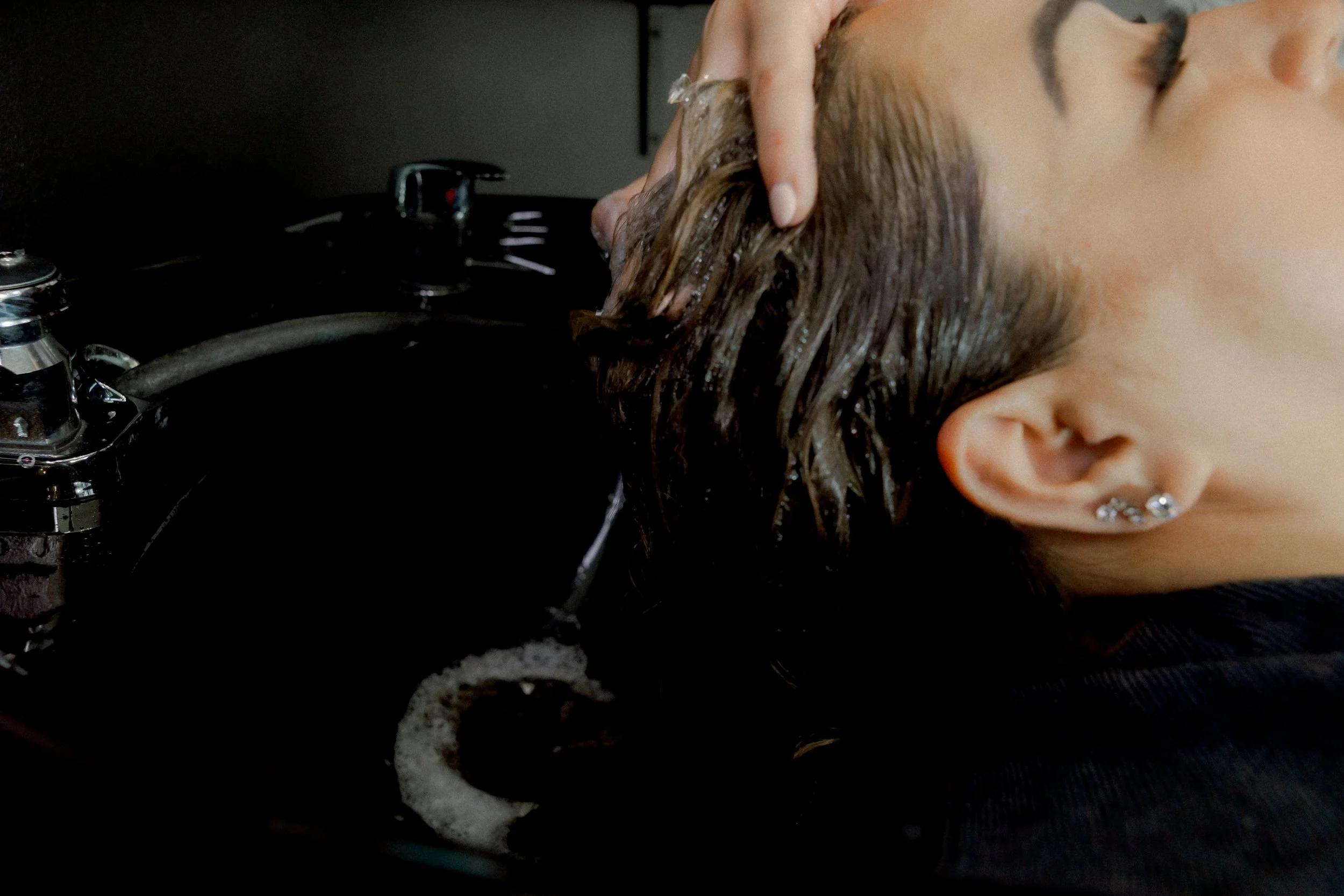 Chelsea's client getting her hair washed in a salon sink with her eyes closed at the Chelsea Extension Co. Salon in Surrey, BC, Canada.