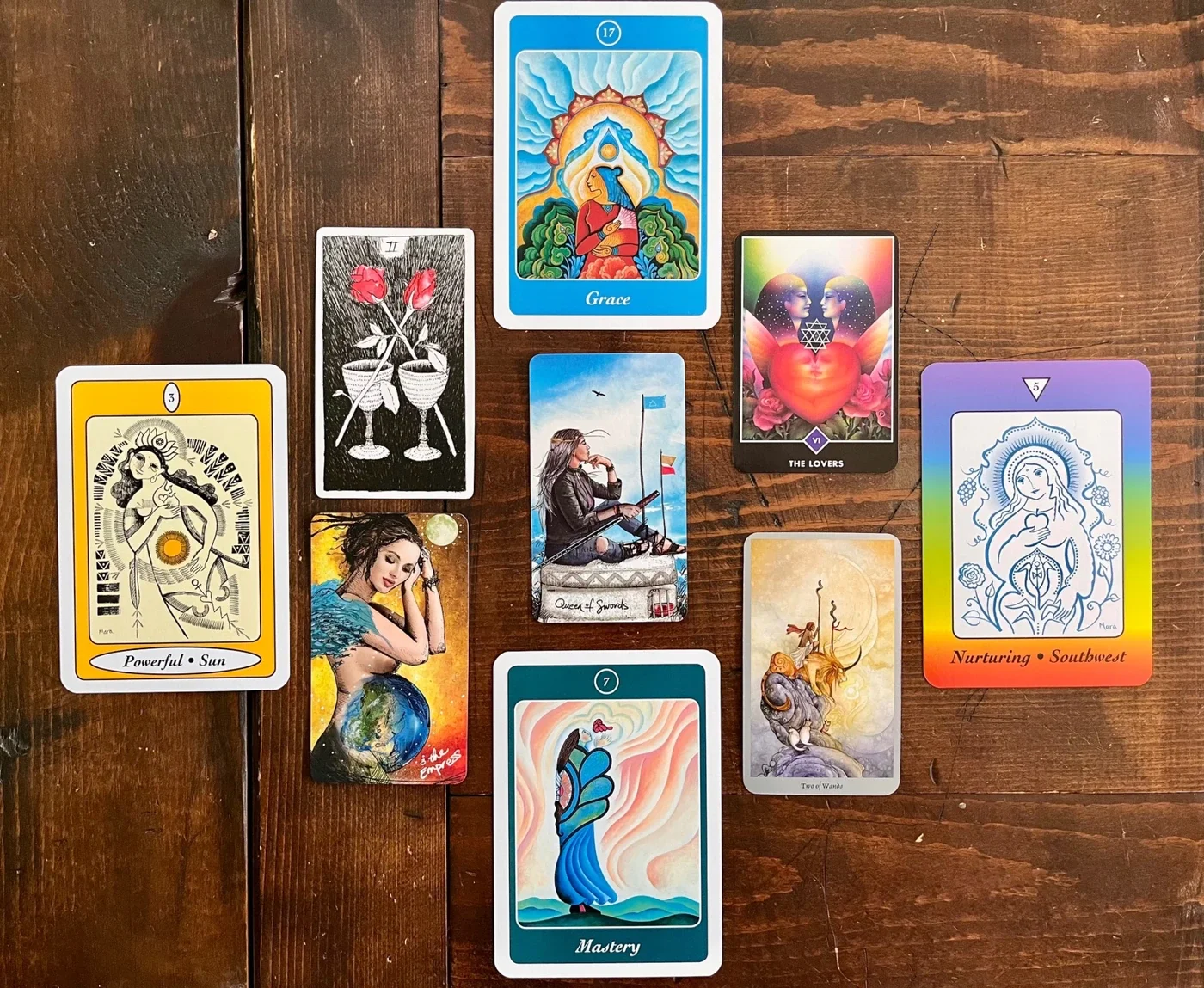 A spread of tarot and oracle cards on a wooden surface, including cards with themes of growth, grace, mastery, nurturing, powerful sun, and love.