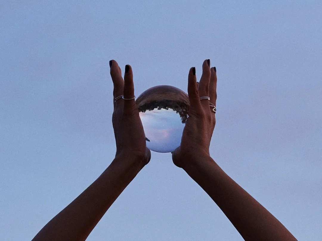 Person holding a reflective glass sphere against a sky background, showing an inverted reflection of the landscape.
