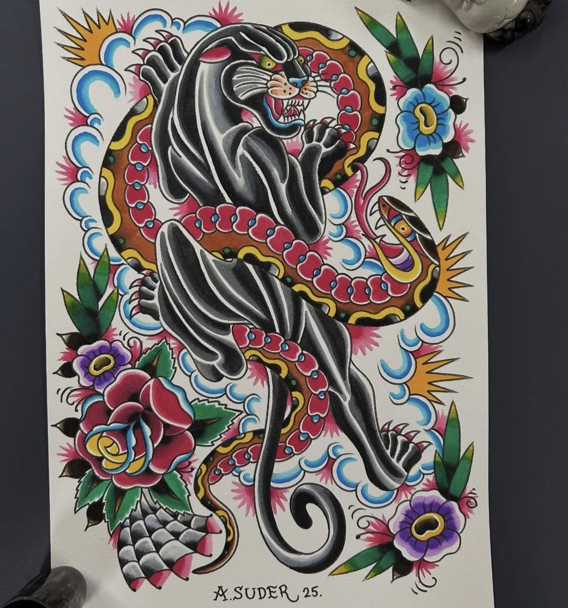 Traditional tattoo-style artwork of a black panther intertwined with a snake, surrounded by colorful flowers and clouds, with the artist's signature A. Suder, age 25.
