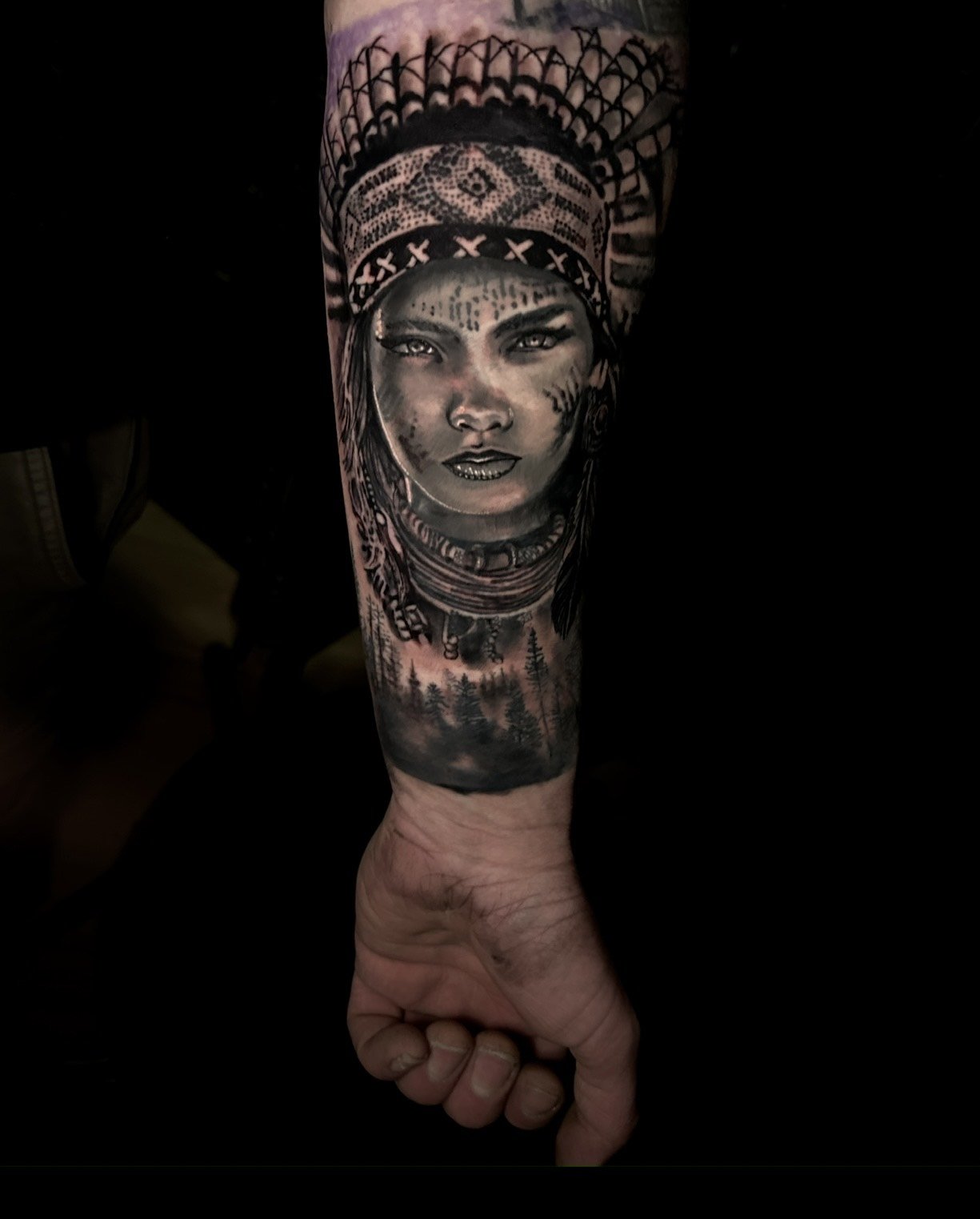 Tattoo of a woman's face with tribal and forest elements on forearm.