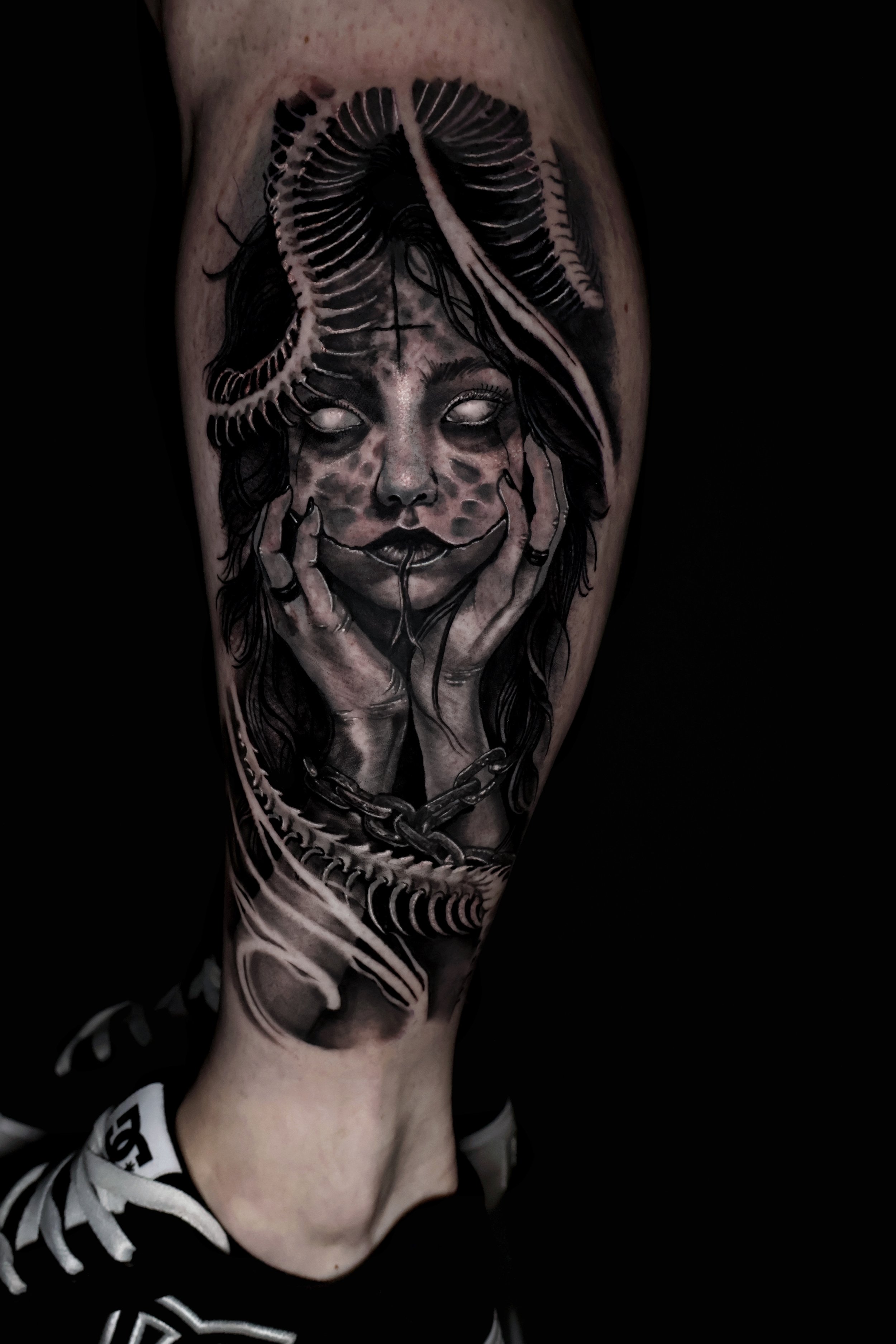 Black and gray tattoo of a woman's face with her eyes closed, hands near her face, and a snake coiled on her head, on a person's arm.