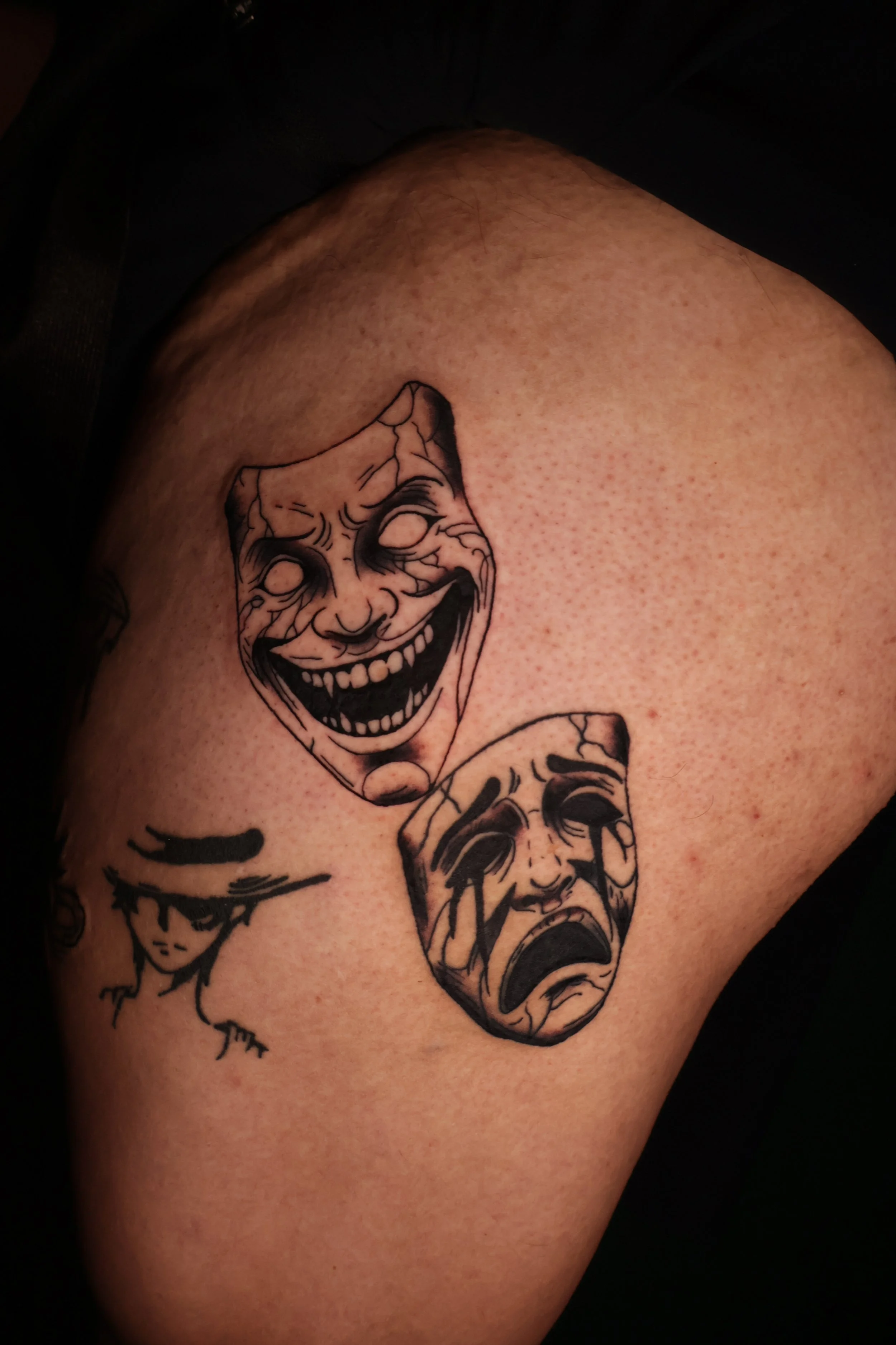 Tattoo of two crying clown faces on a person's upper arm.