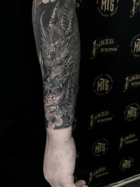 Close-up of a person's arm with a detailed black and gray tattoo of a dragon.