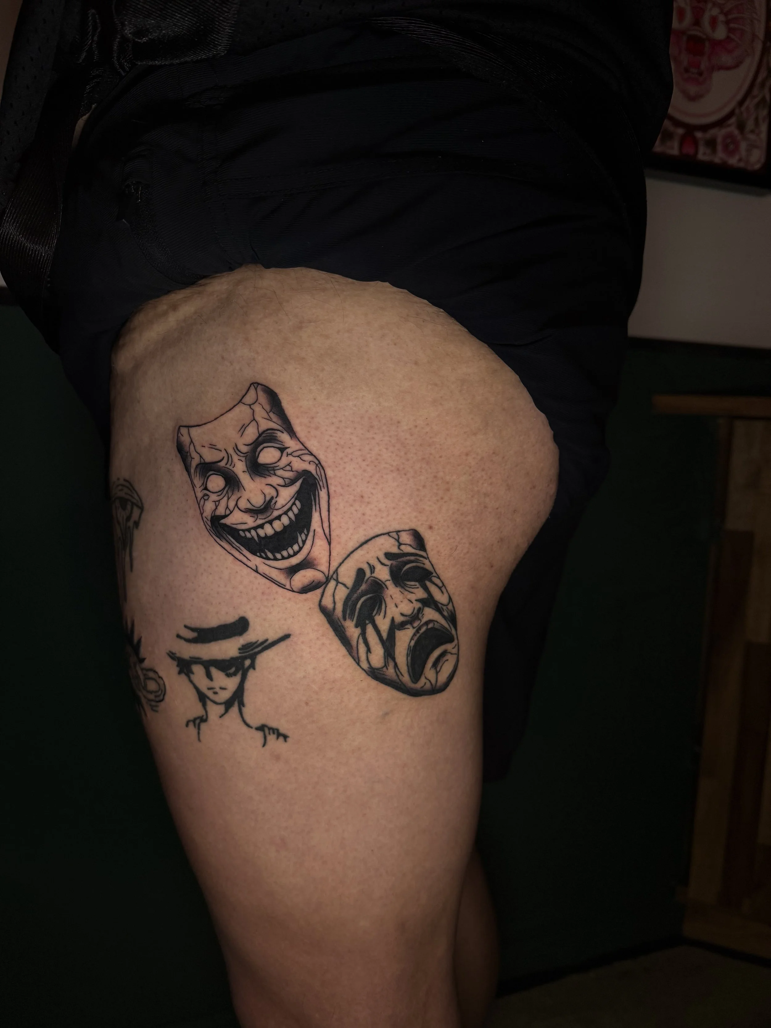 Close-up of a person's thigh with a tattoo of a smiling clown face.