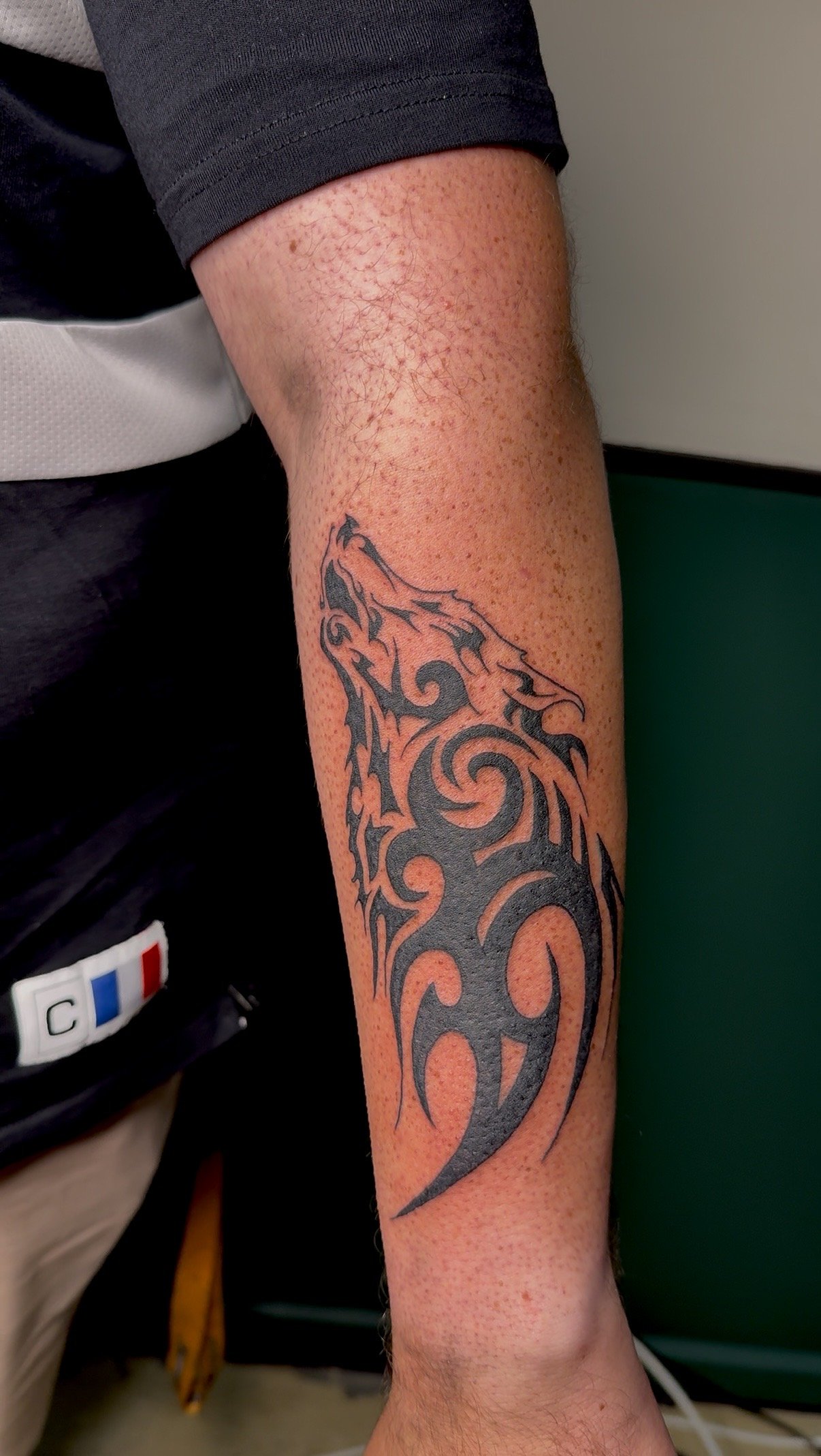 A person's arm with a tribal-style tattoo, featuring sharp curves and swirling patterns.