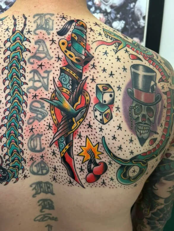 Colorful tattoo on upper chest featuring a serpent, a skull with a top hat, dice, a cherry, and decorative stars.