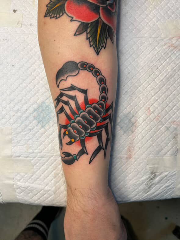 Tattoo of a black and red scorpion on a person's forearm.