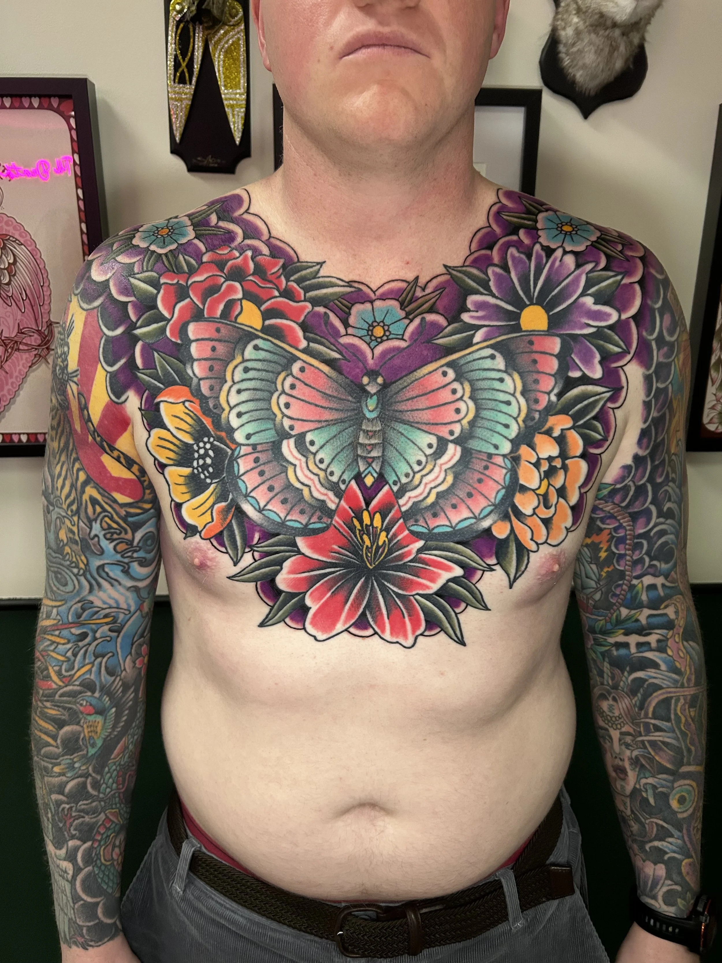 A tattooed man with extensive colorful tattoos on his chest and arms, including a large butterfly and floral patterns.