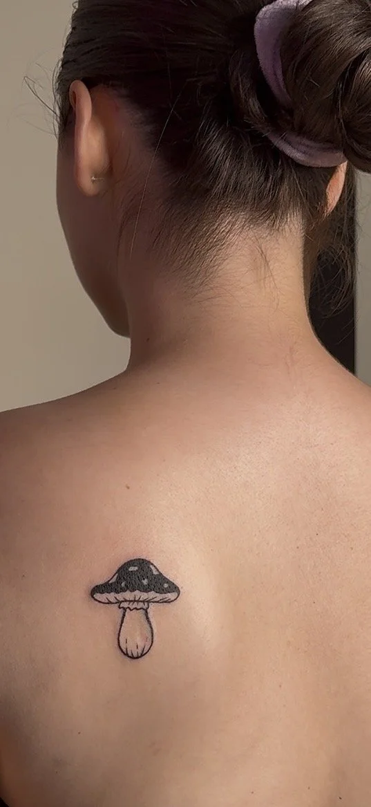 Back of a woman with a mushroom tattoo on her upper back.