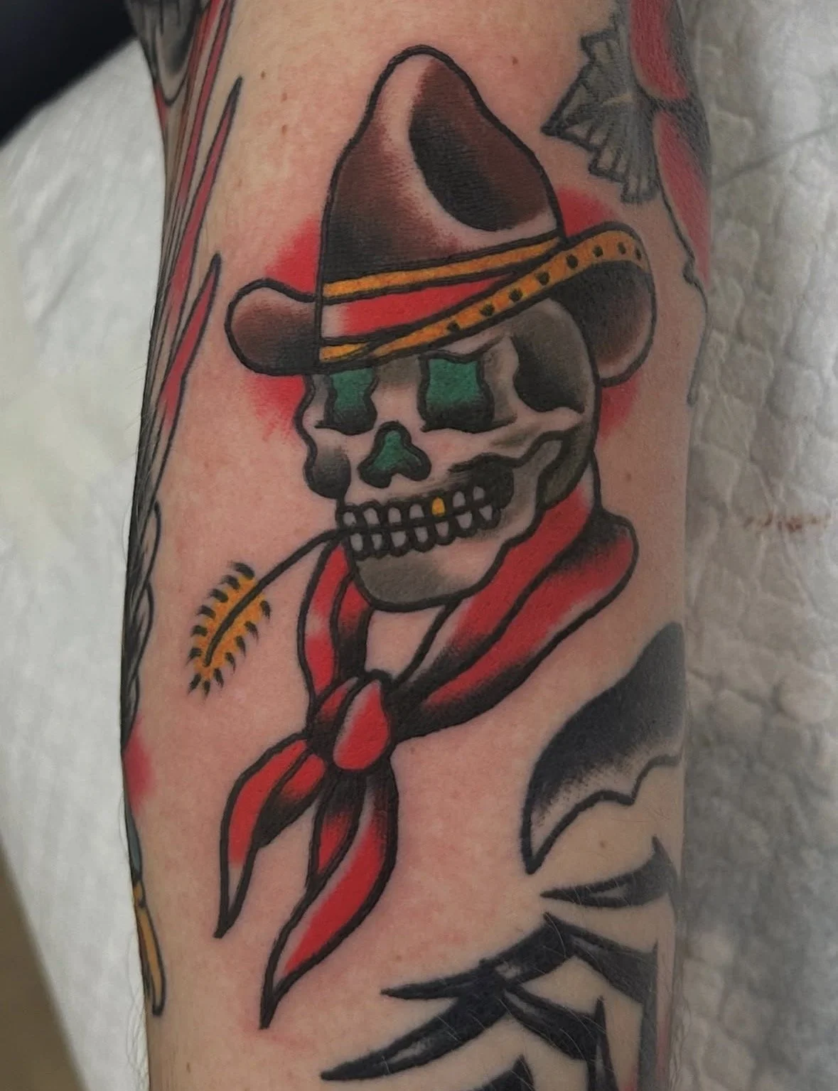 Tattoo of a skull with a cowboy hat, cigarette in mouth, and a red bandana around neck.