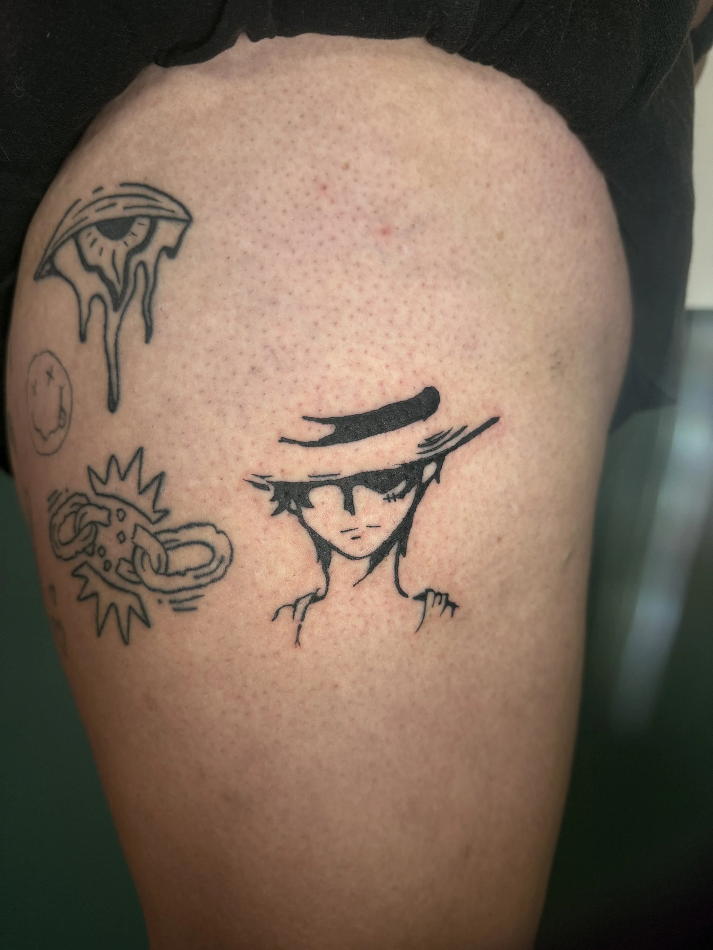 Tattoo of a girl with closed eyes, flowers, a smiling sun, a dripping eye, and other designs on a person's shoulder.
