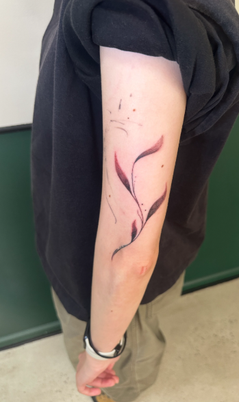 Tattoo of a pink and black abstract flower or leaf design on person's upper arm.