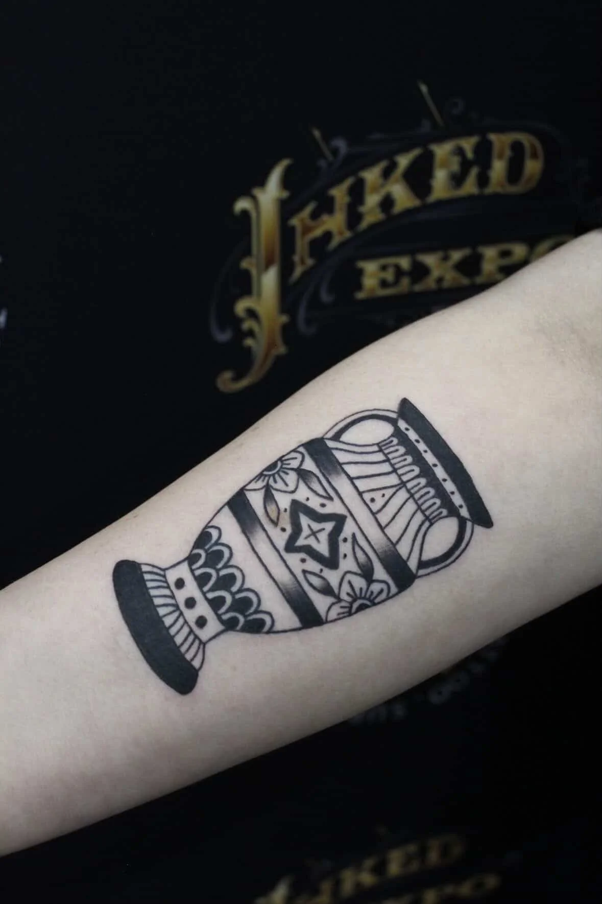 Black outline tattoo of a vintage vase with decorative patterns on a person's arm.