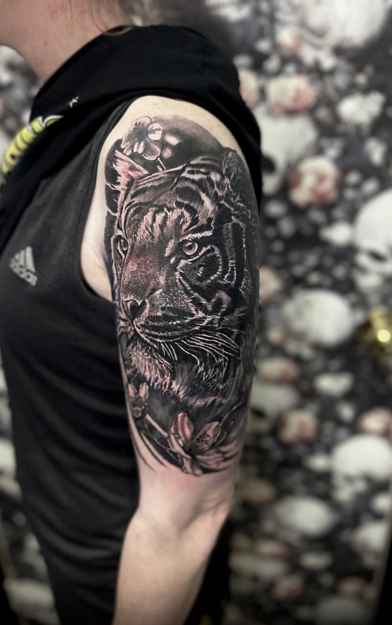 Tattoo of a tiger's face on a person's upper arm, with floral and nature elements surrounding it.