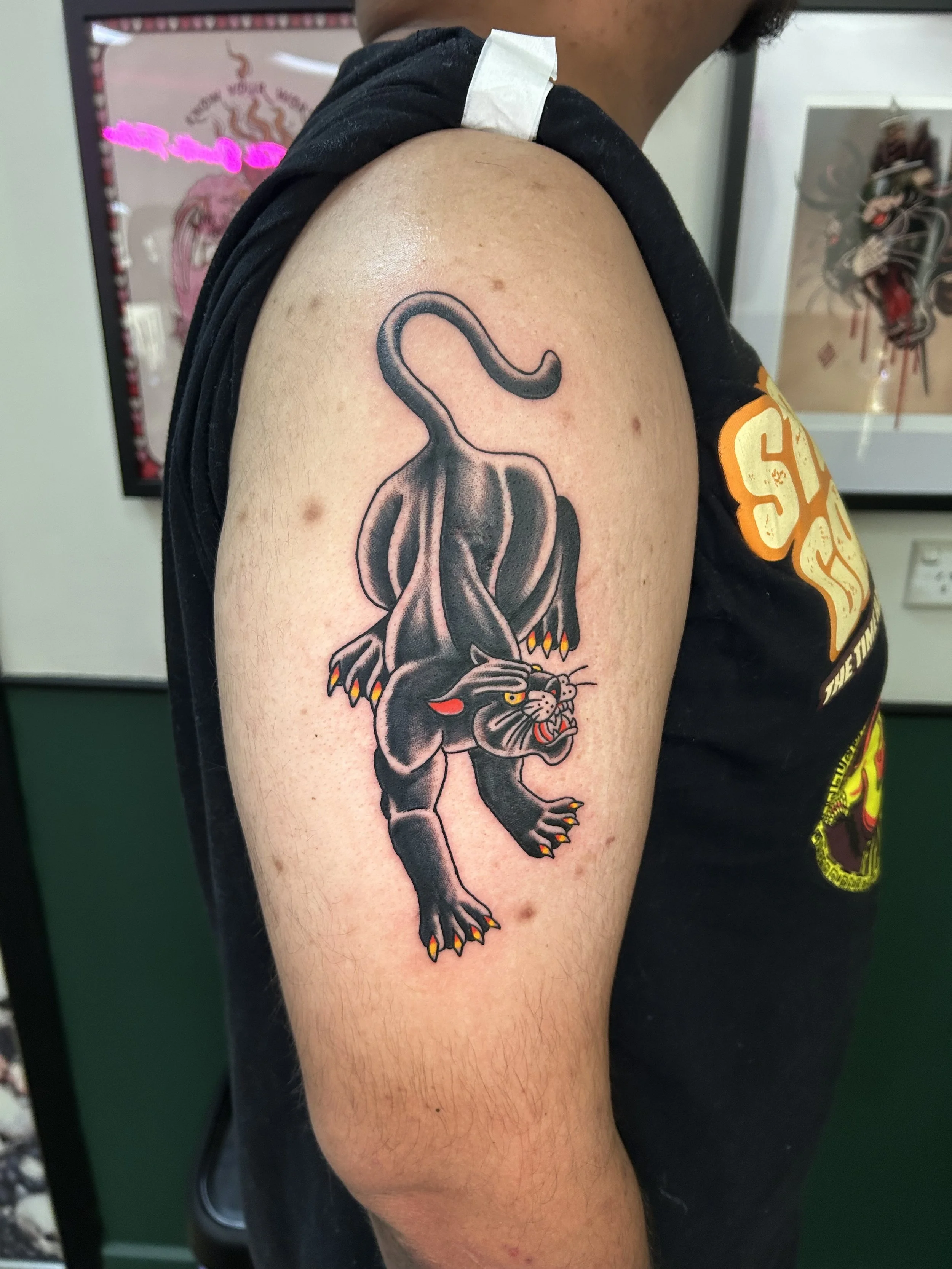 Tattoo of a black panther with yellow eyes and red tongue, crouching on the upper arm of a person.