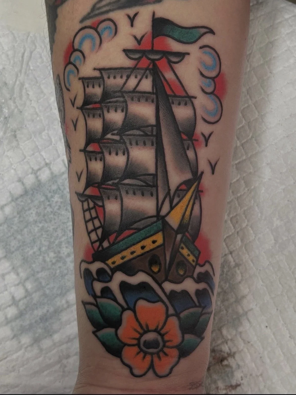 Tattoo of a traditional sailing ship with billowing sails, surrounded by waves, a large orange flower at the bottom, and clouds in the background.