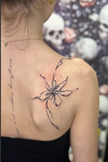 Tattoo of a flower on the upper shoulder of a person with dark hair.