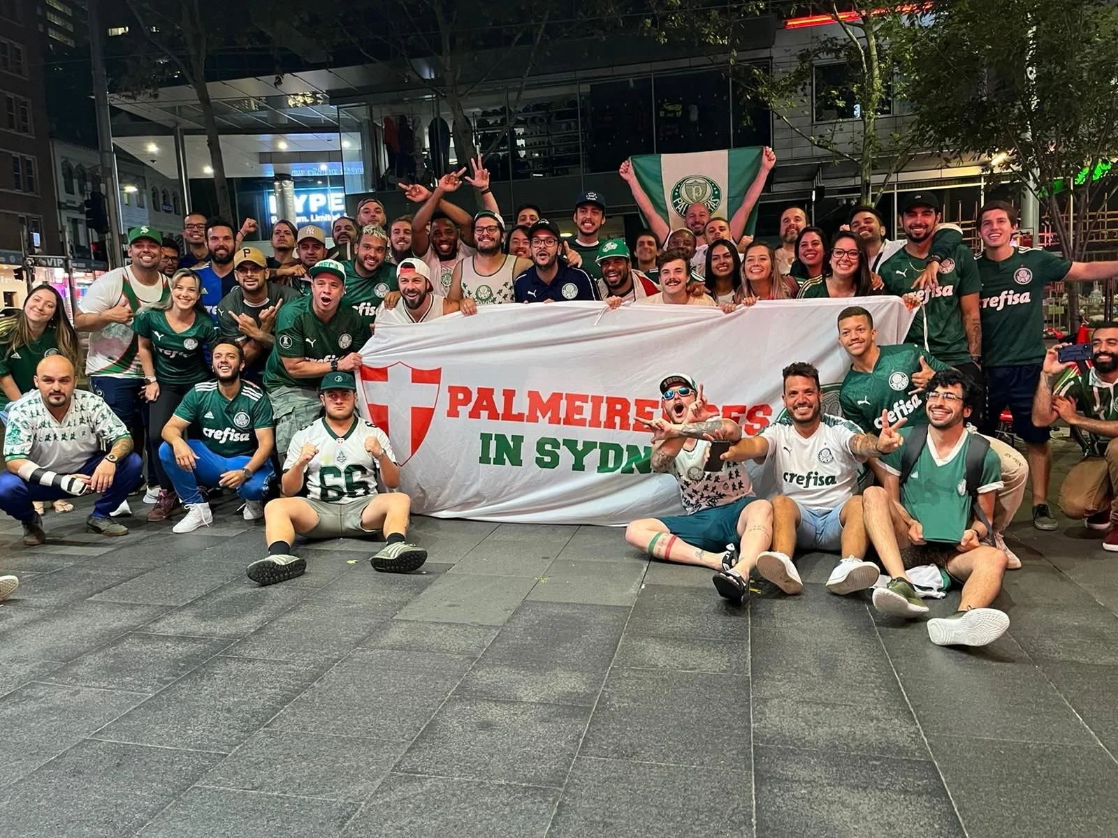 Group of people wearing green and white soccer jerseys celebrating inside a restaurant or bar.