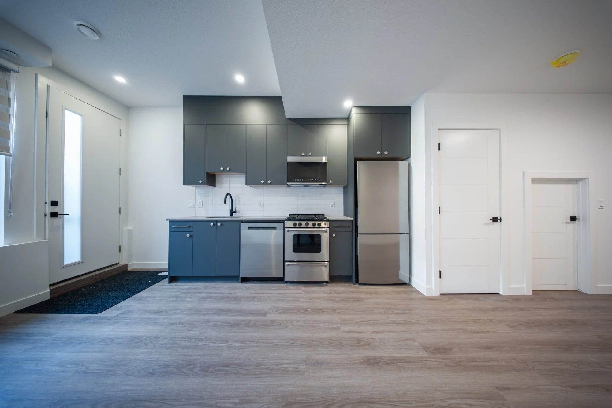 Modern kitchen with blue cabinets, stainless steel appliances, and white walls with wood flooring.