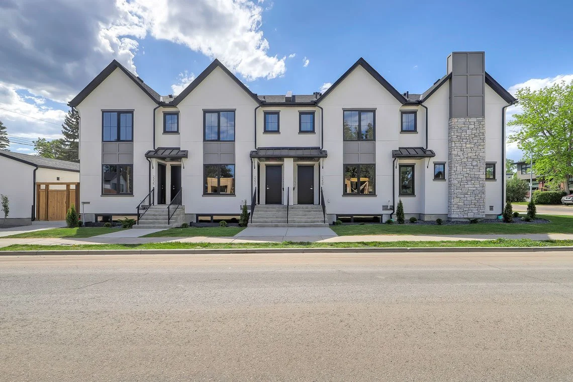 Modern multi-family residential building with three units, white exterior, black window frames, stone chimney, and front porches with steps