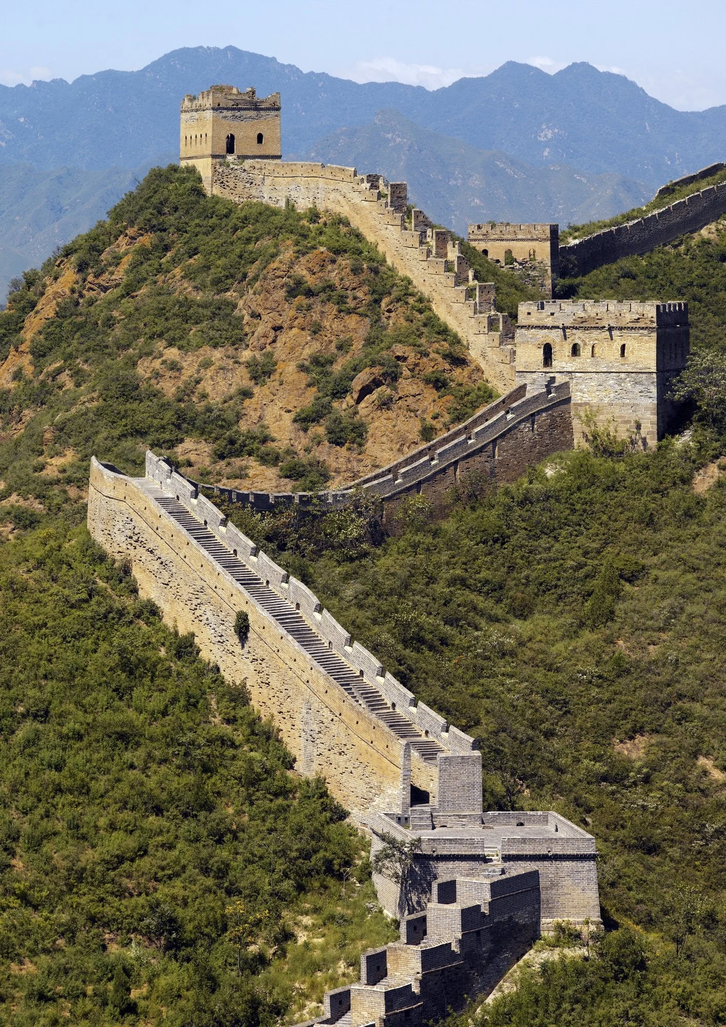 The Great Wall of China winding through green mountains under a blue sky.