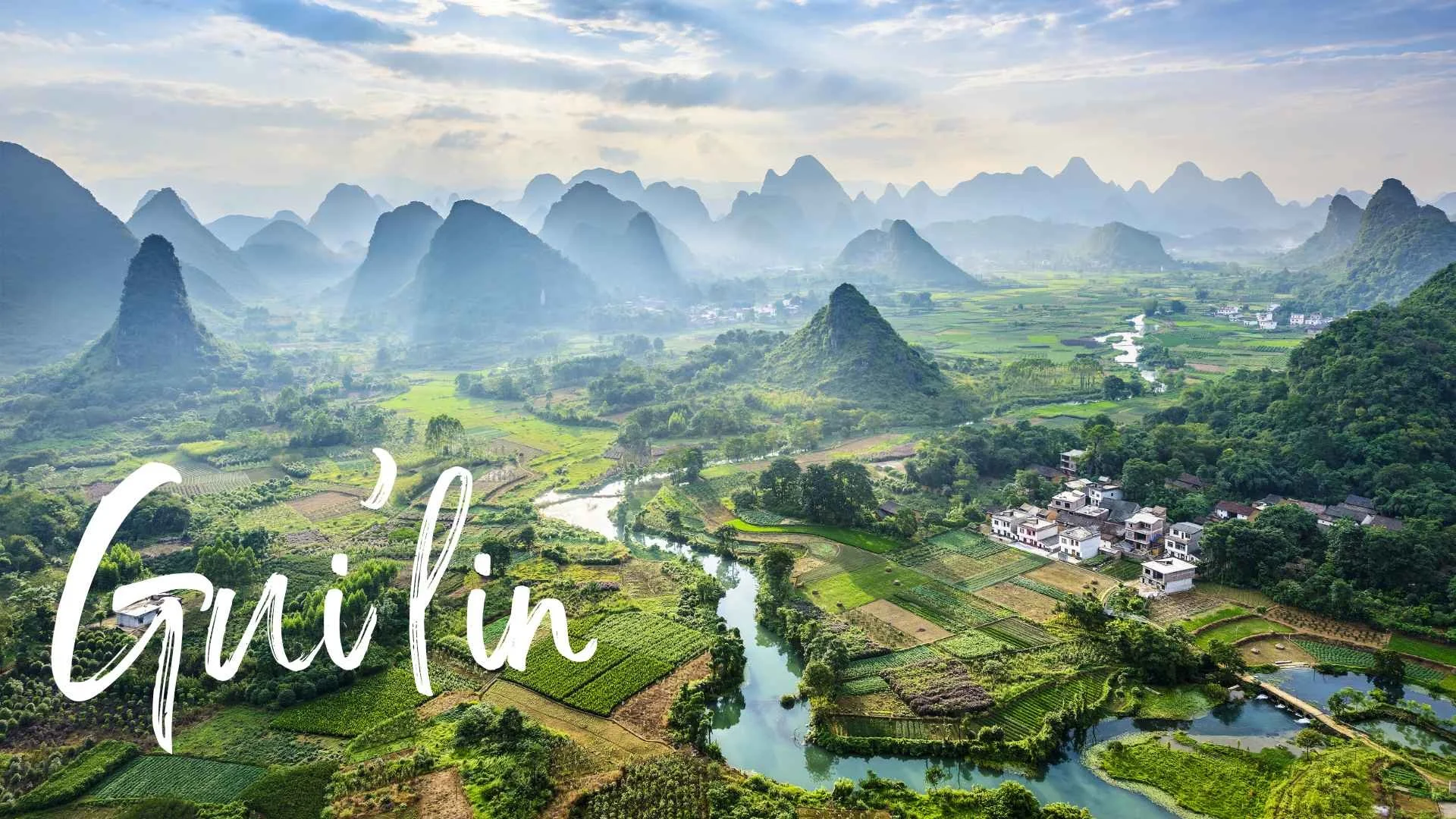 Scenic view of a lush green valley with river, farm fields, and small white buildings, surrounded by rocky mountains under a partly cloudy sky with the text 'Guilin' overlayed.