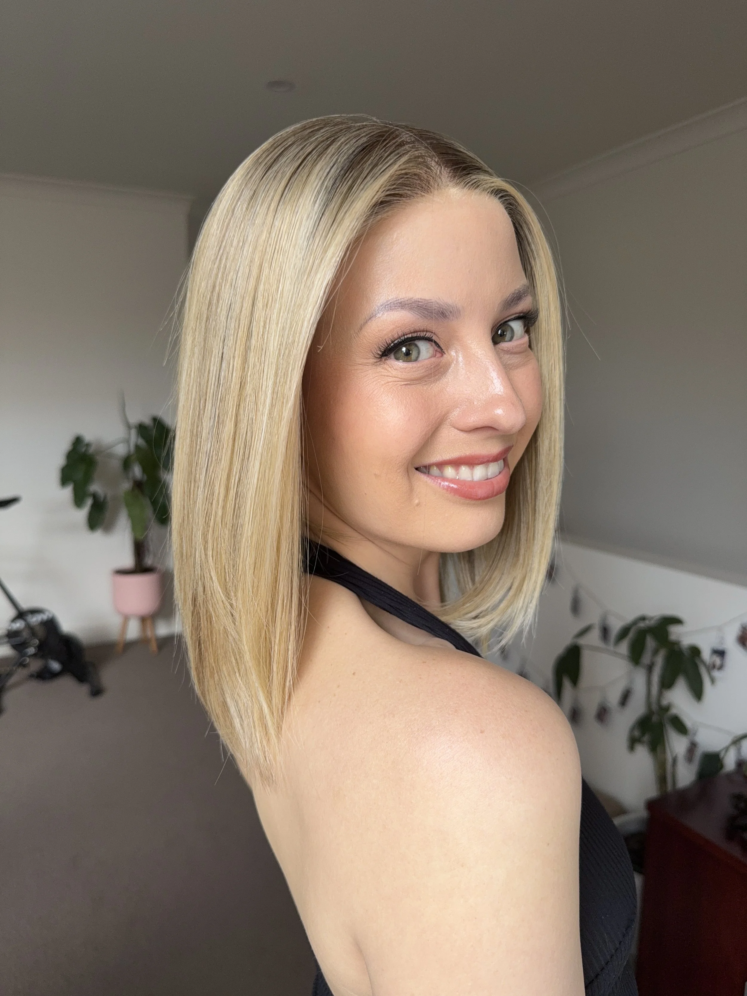 A woman with shoulder-length blonde hair smiling at the camera indoors.