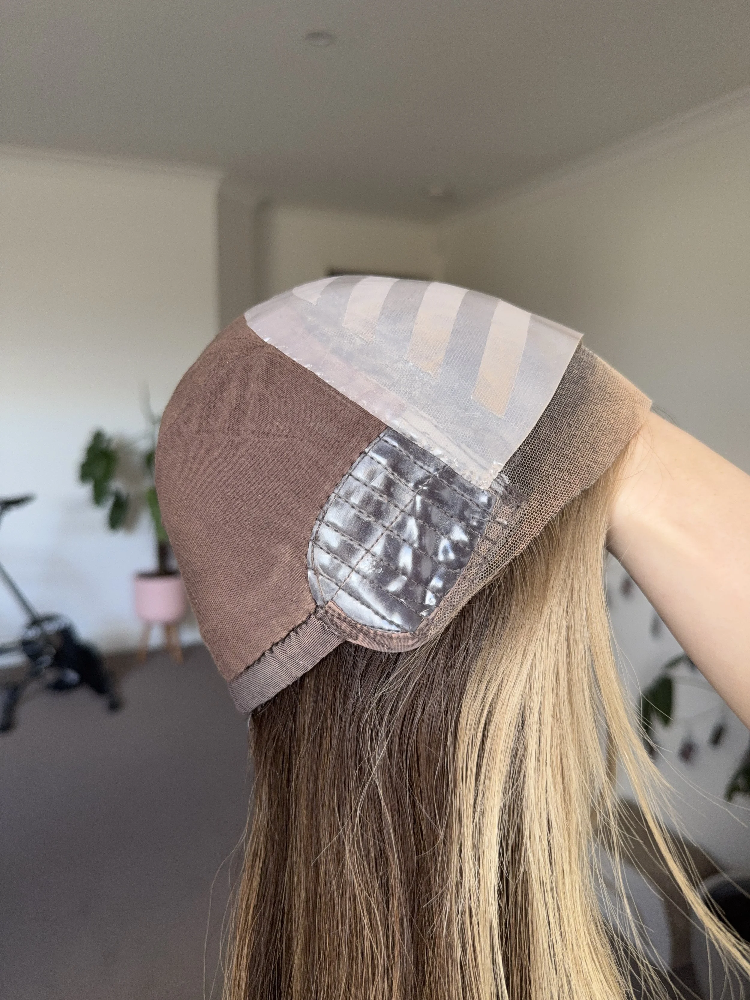 A wig cap with different fabric patches, including brown, beige, gray, white, and a shiny gray pattern, covers a blonde mannequin head.