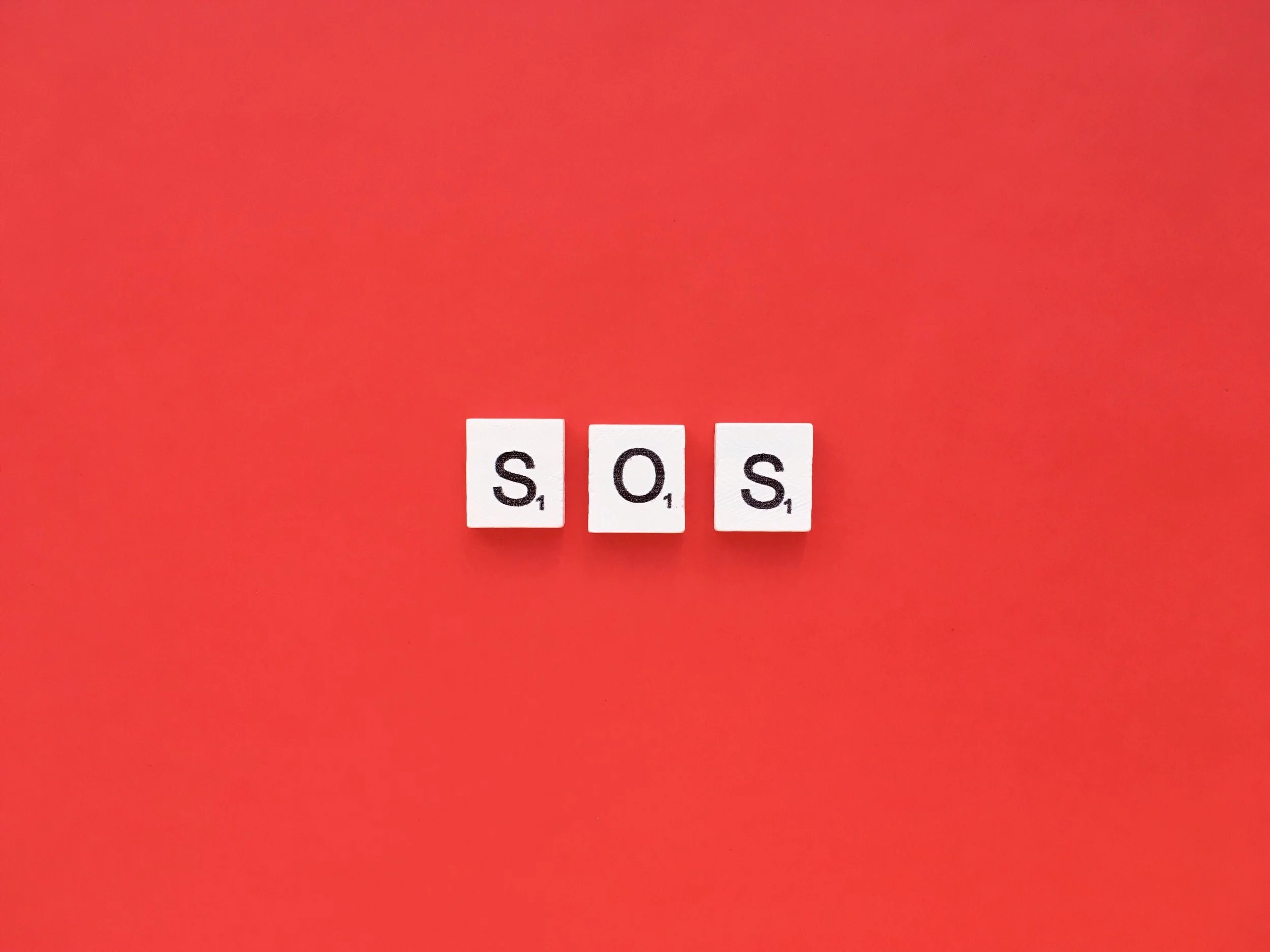 Three Scrabble tiles spelling out 'SOS' on a red background.