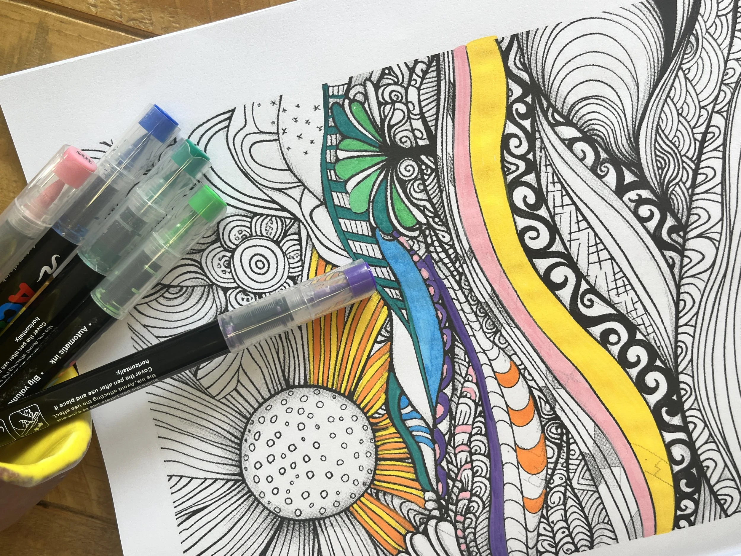 A colorful abstract drawing on a sheet of paper with black stamp markers and a yellow holder nearby.