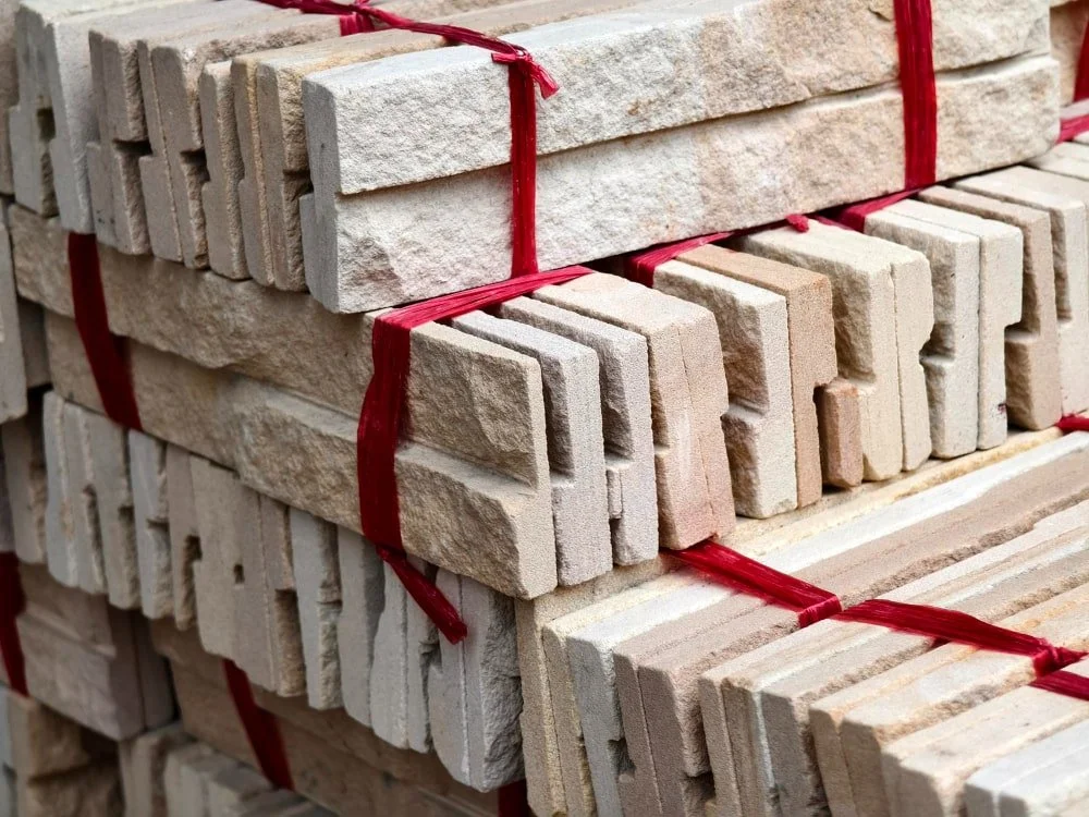 Stacks of beige stone bricks tied with red plastic straps on a pallet.
