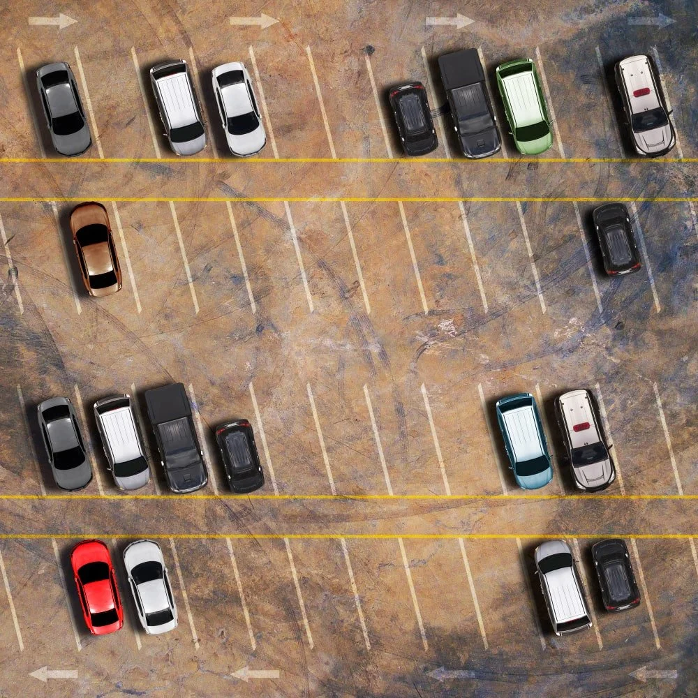 Top-down view of a parking lot with several parked cars, some parked within lines and others outside, with empty spaces and a concrete surface.