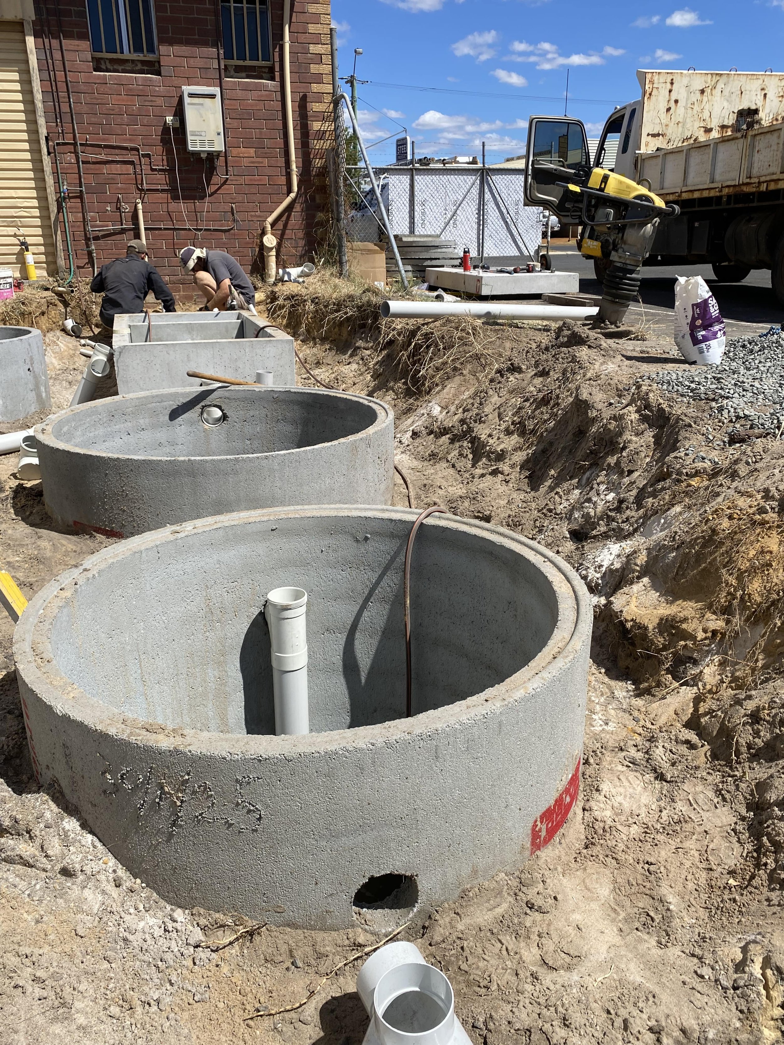 Construction site with underground concrete septic tanks, workers, and construction equipment under a blue sky.