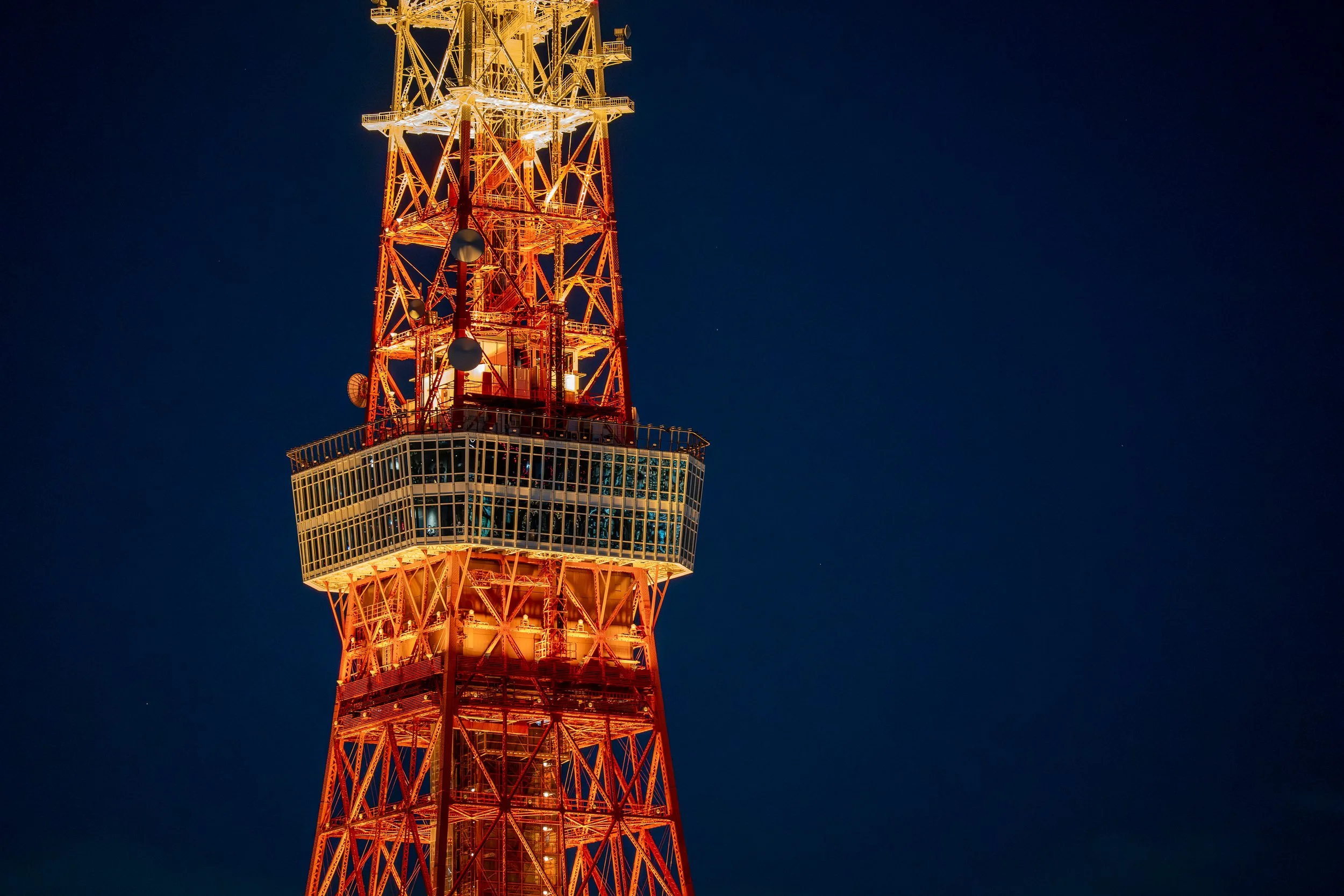 A nighttime view of a red and white radio tower illuminated against a dark blue sky.