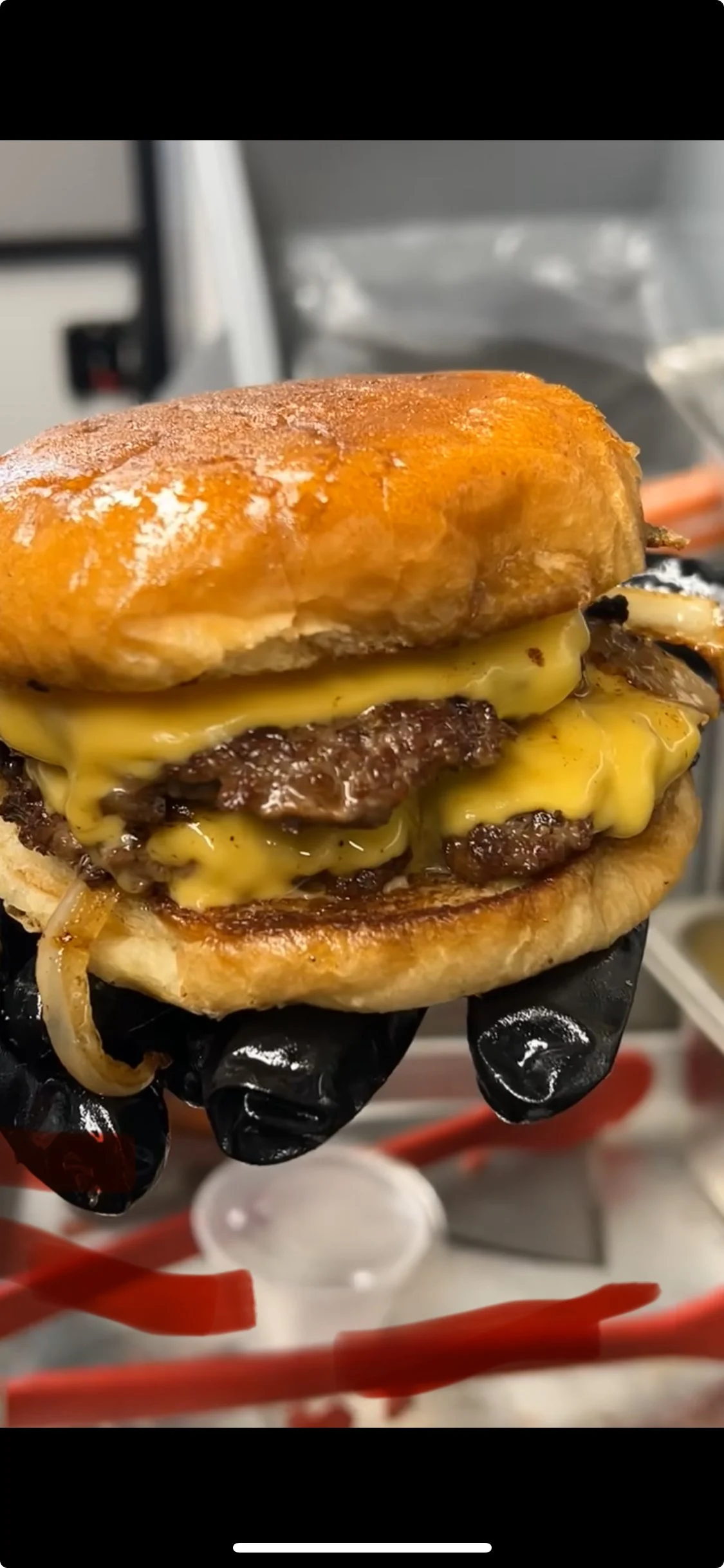 Close-up of a cheeseburger with melted cheese, beef patty, and toasted bun, held with black disposable gloves.
