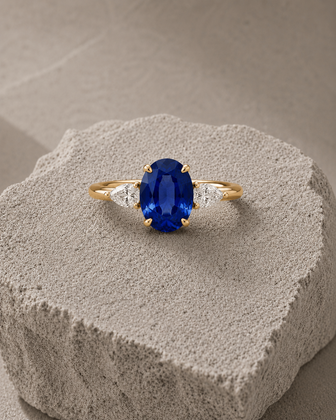 Gold ring with a royal blue oval gemstone flanked by two clear pear-shaped stones on a natural rock background.