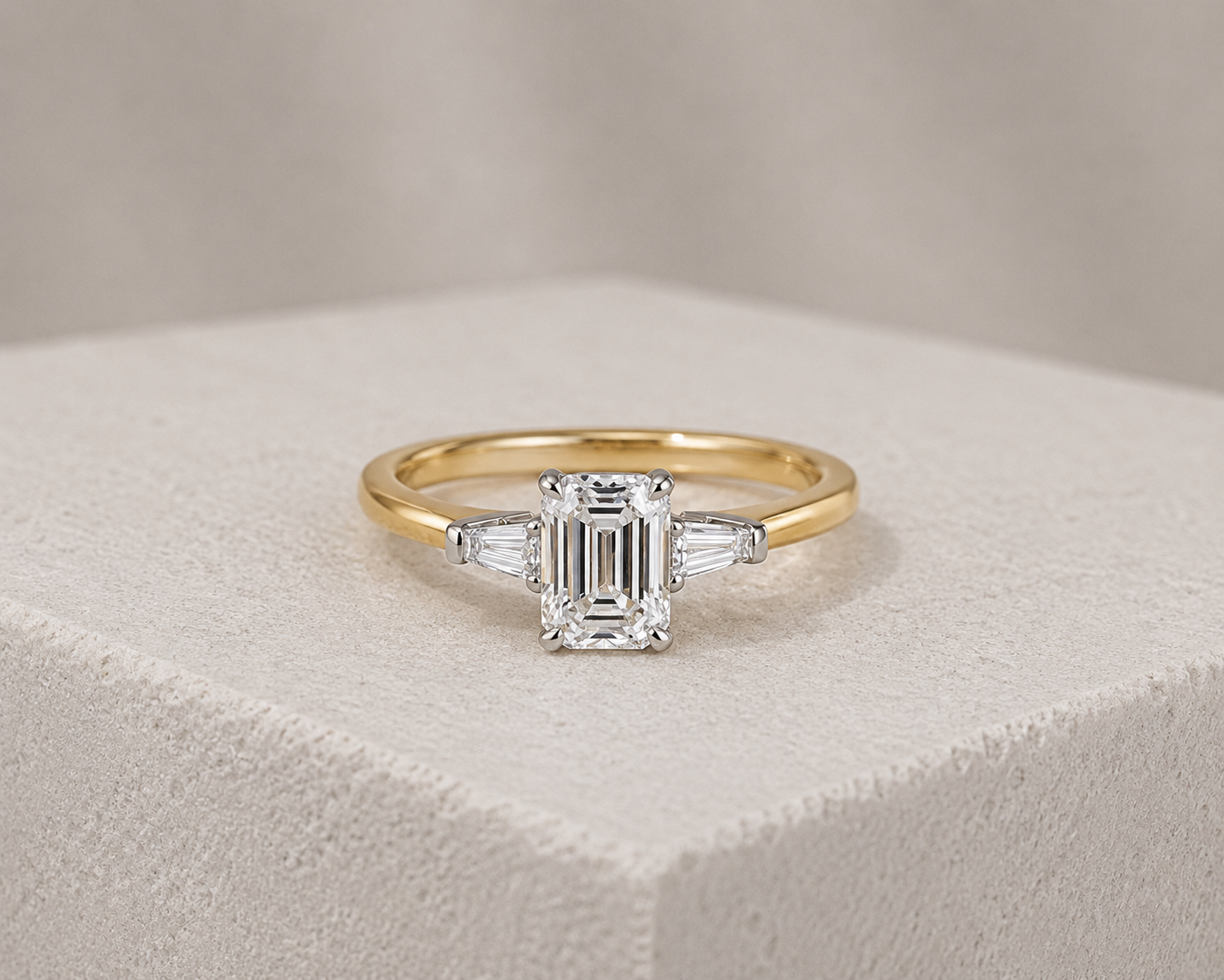 Gold ring with a large emerald-cut diamond center stone flanked by two tapered baguette diamonds.