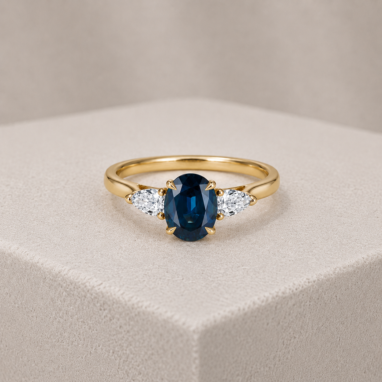 Gold ring with a dark blue oval gemstone flanked by two clear pear-shaped stones on a white background.