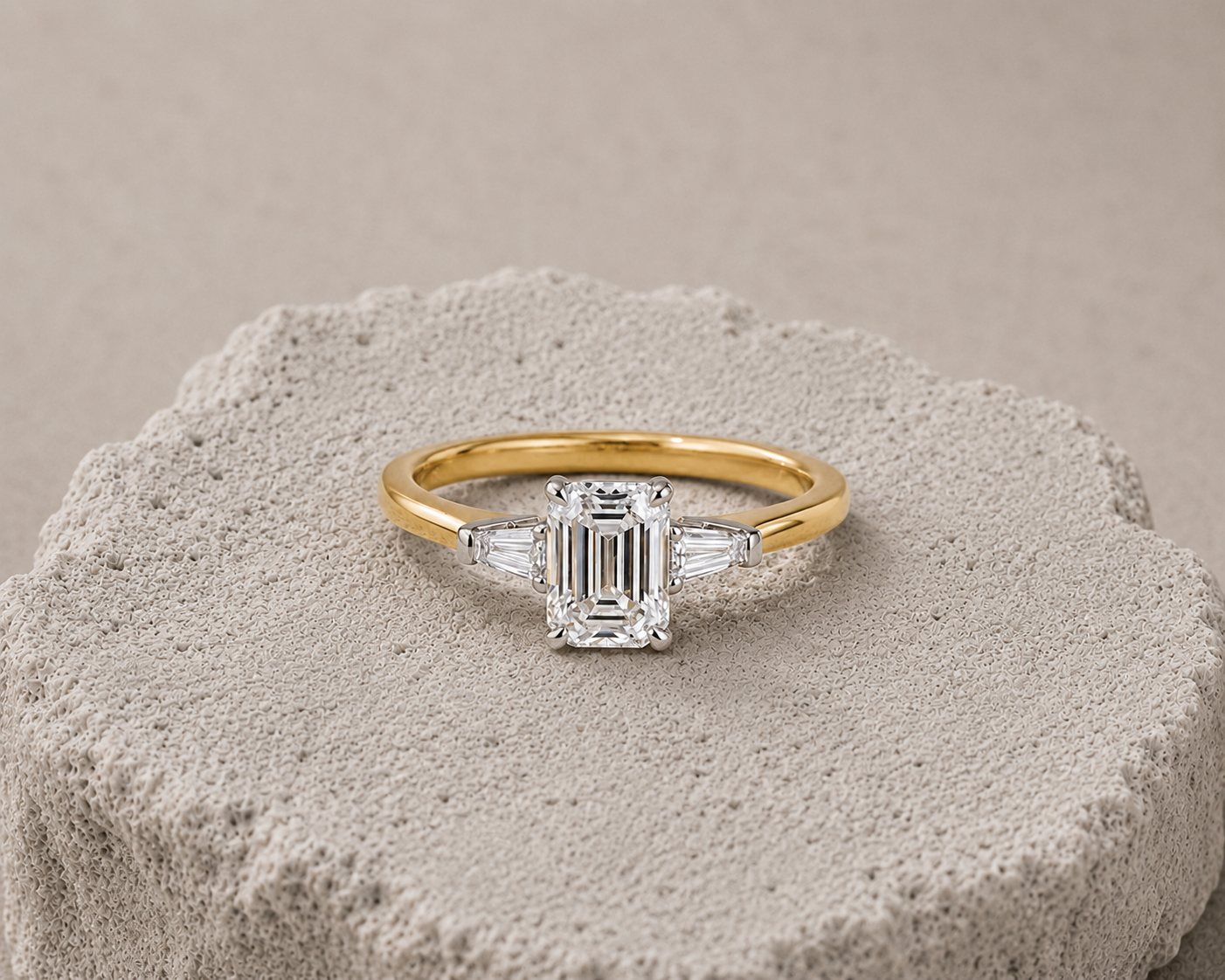 Gold ring with a large emerald-cut diamond center stone flanked by two tapered baguette diamonds.