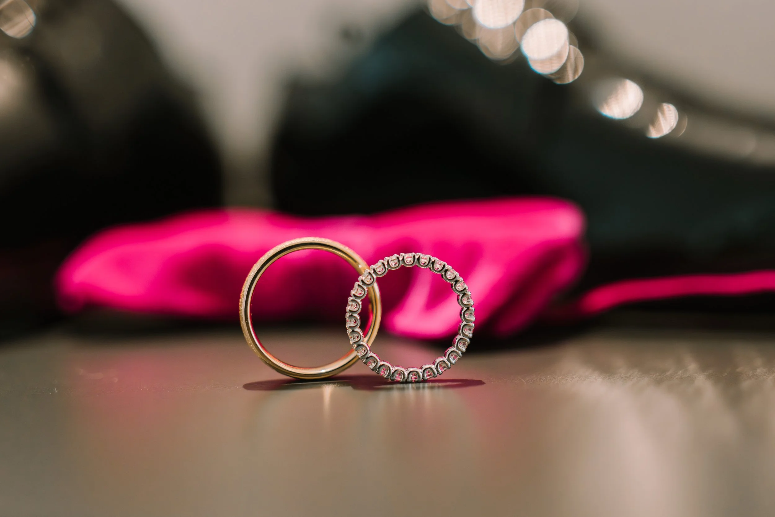 Verlobungsring aus Gold und ein Ehering mit Diamanten auf einem Tisch mit pinker Schleife im Hintergrund.